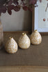 Three small textured ochre bud vases on a textured surface with a neutral background