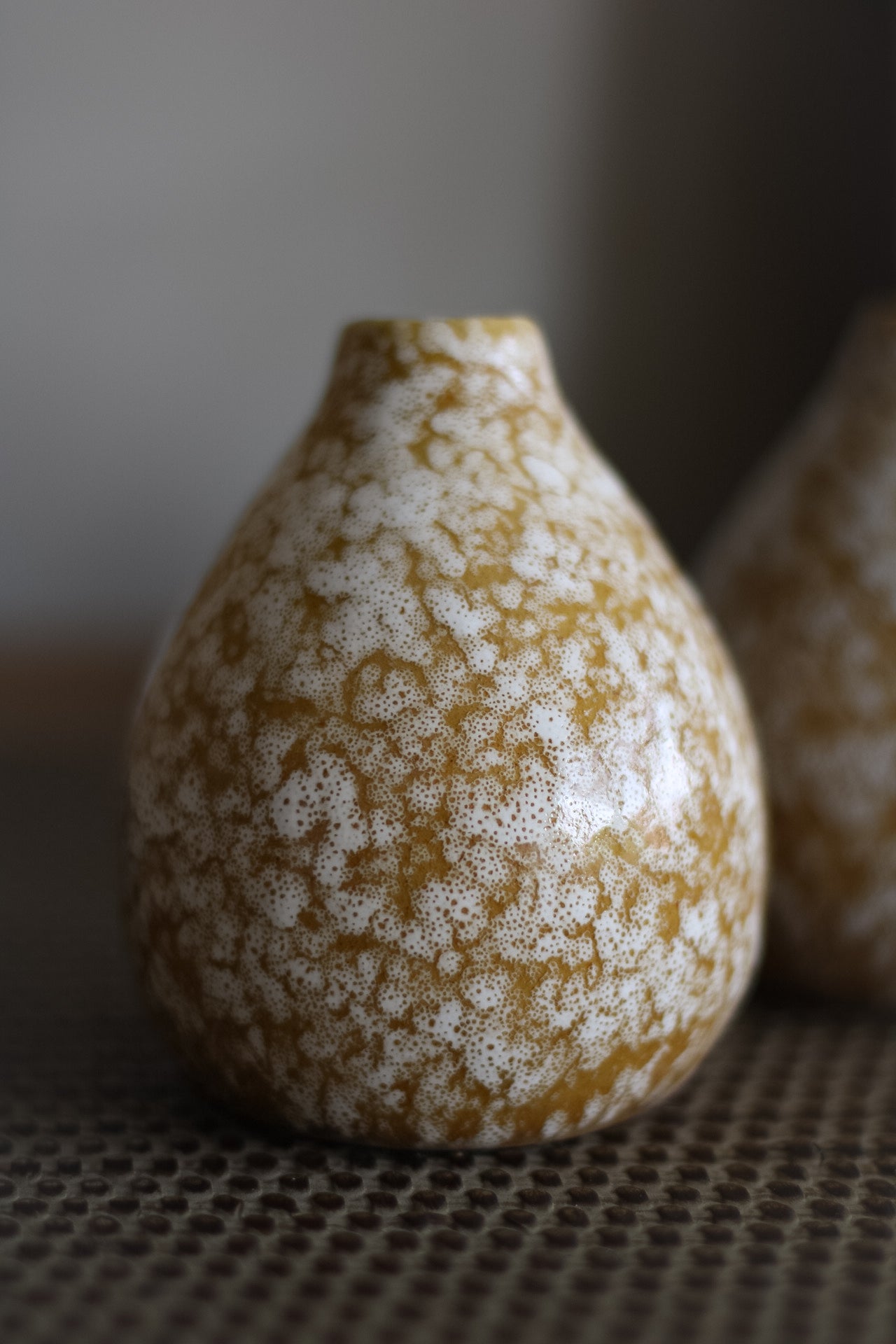 Decorative ceramic bud vase with speckled pattern on a textured surface