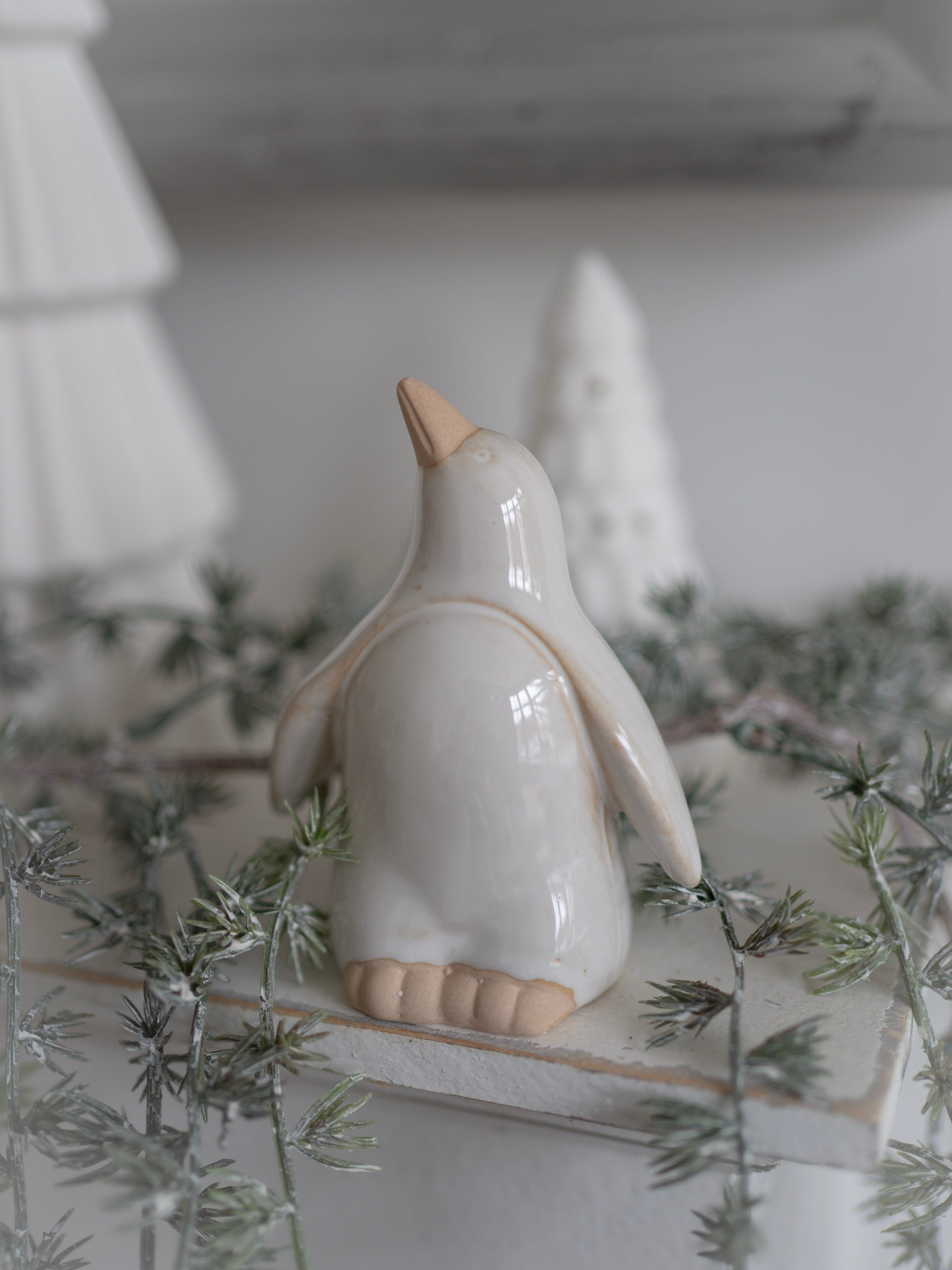 White ceramic penguin figurine on a white surface with decorative elements