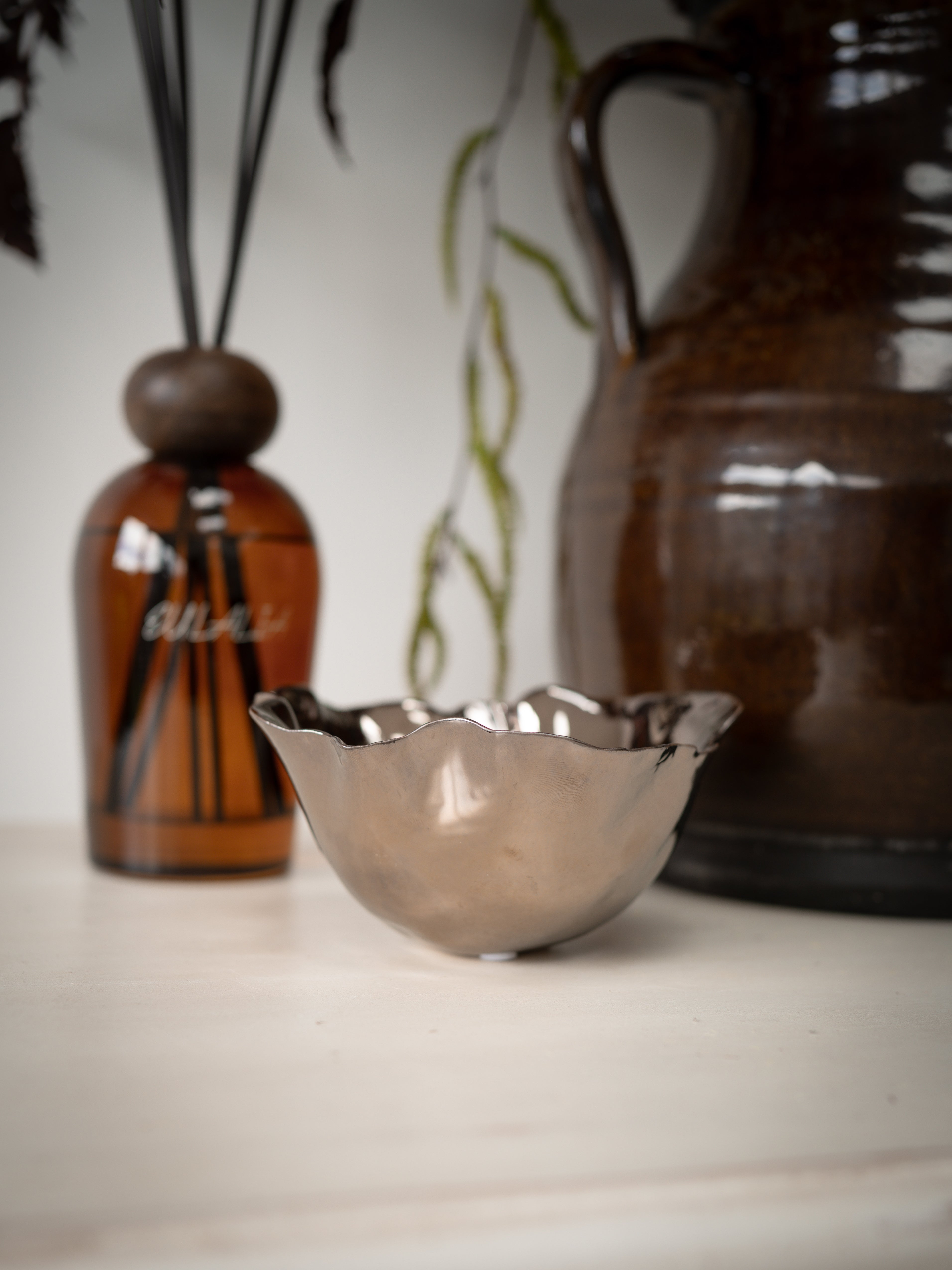 Copper bowl on a surface with a blurred background featuring a bottle and a vase.