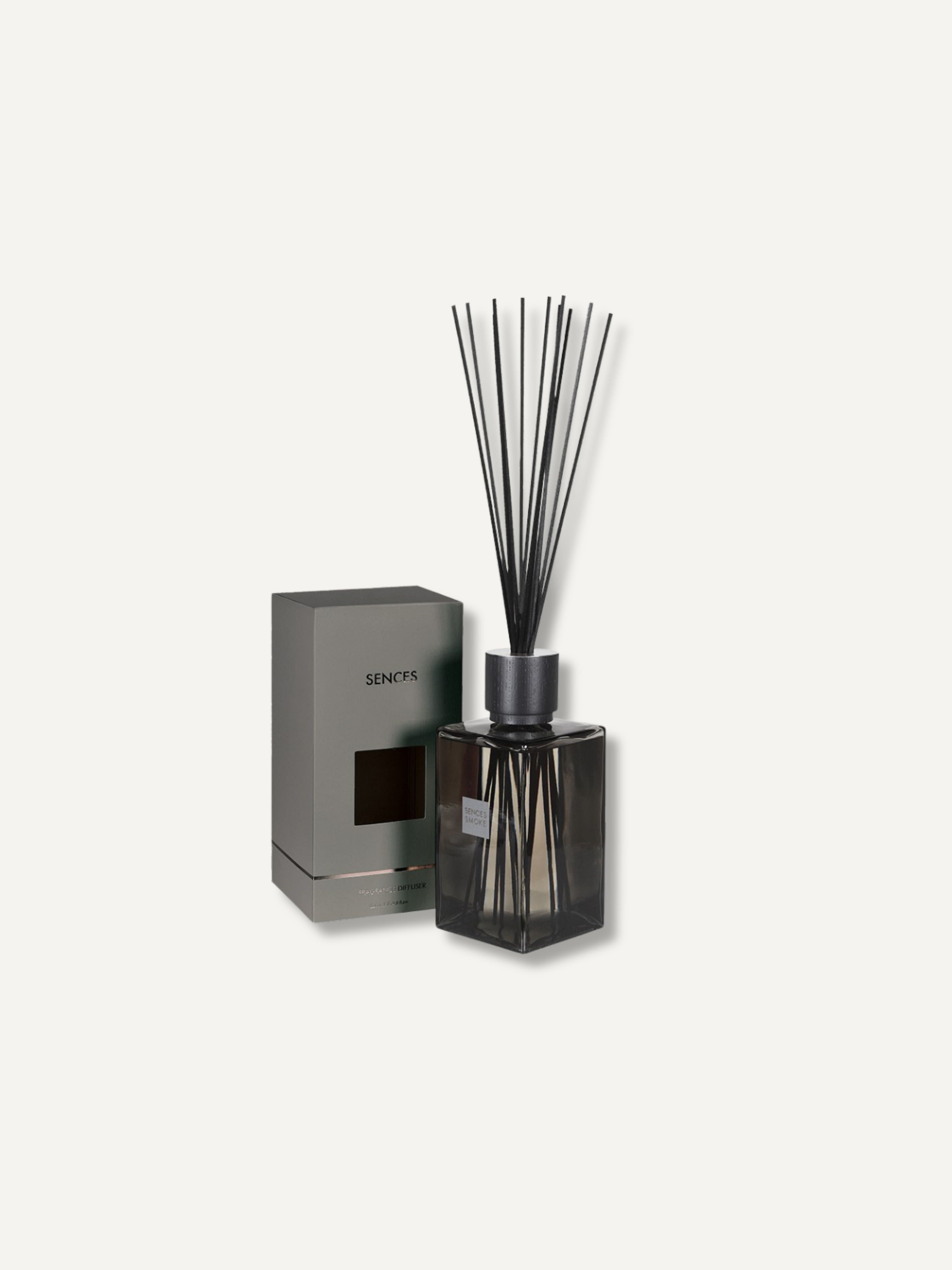 A reed diffuser bottle with dark glass and black reeds, shown next to its gray rectangular box on a plain light background.