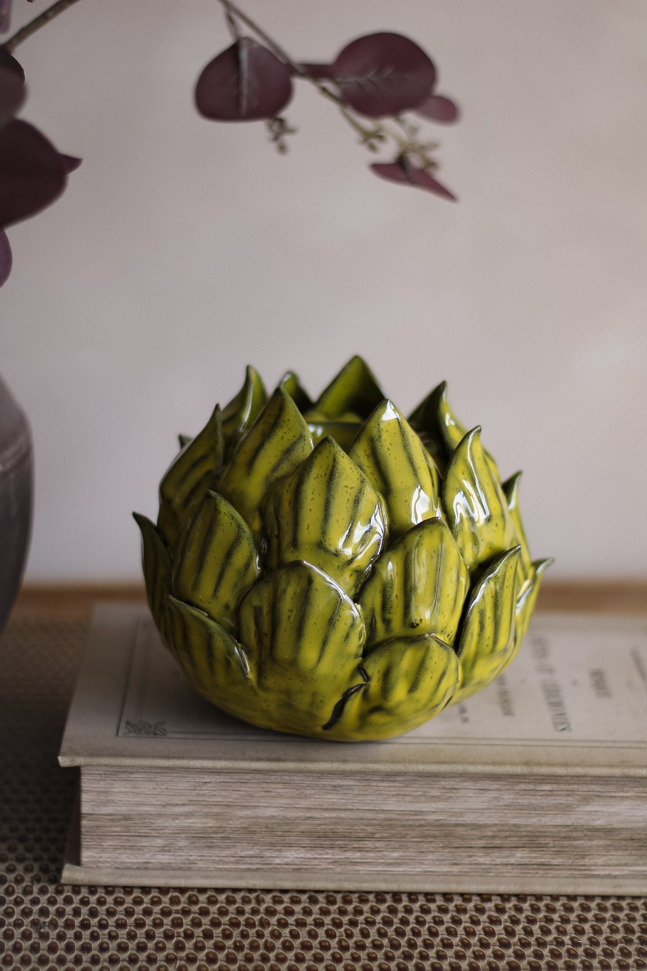 Green ceramic artichoke-shaped vase on a stack of books with a neutral background