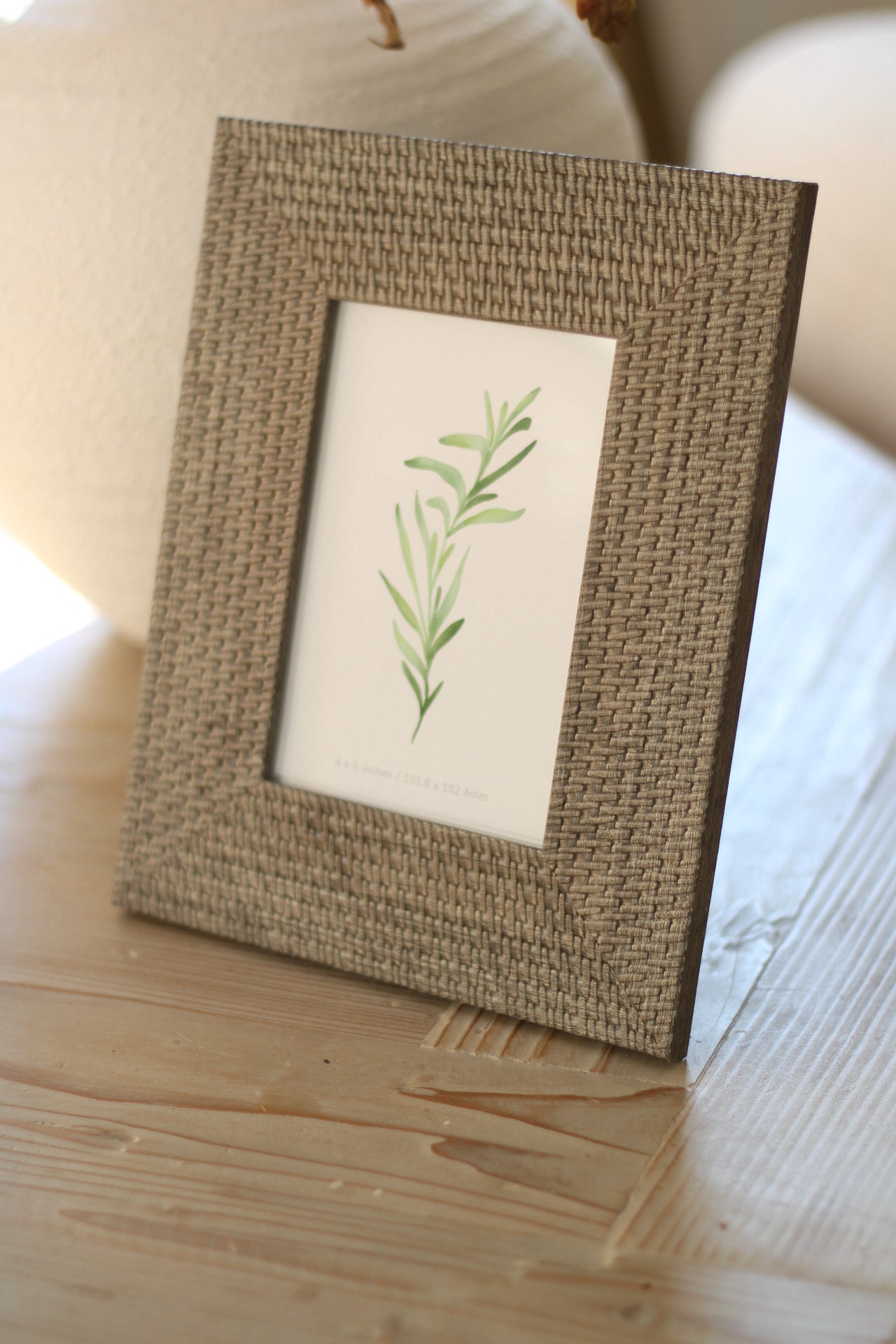 Soft grey woven photo frame with a green leaf design on a wooden surface