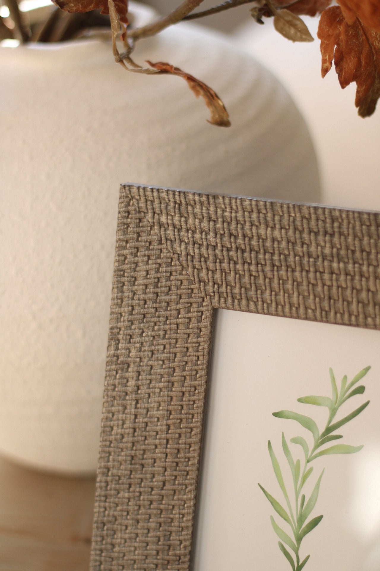 Close-up of a woven frame with a plant-themed print on a neutral background