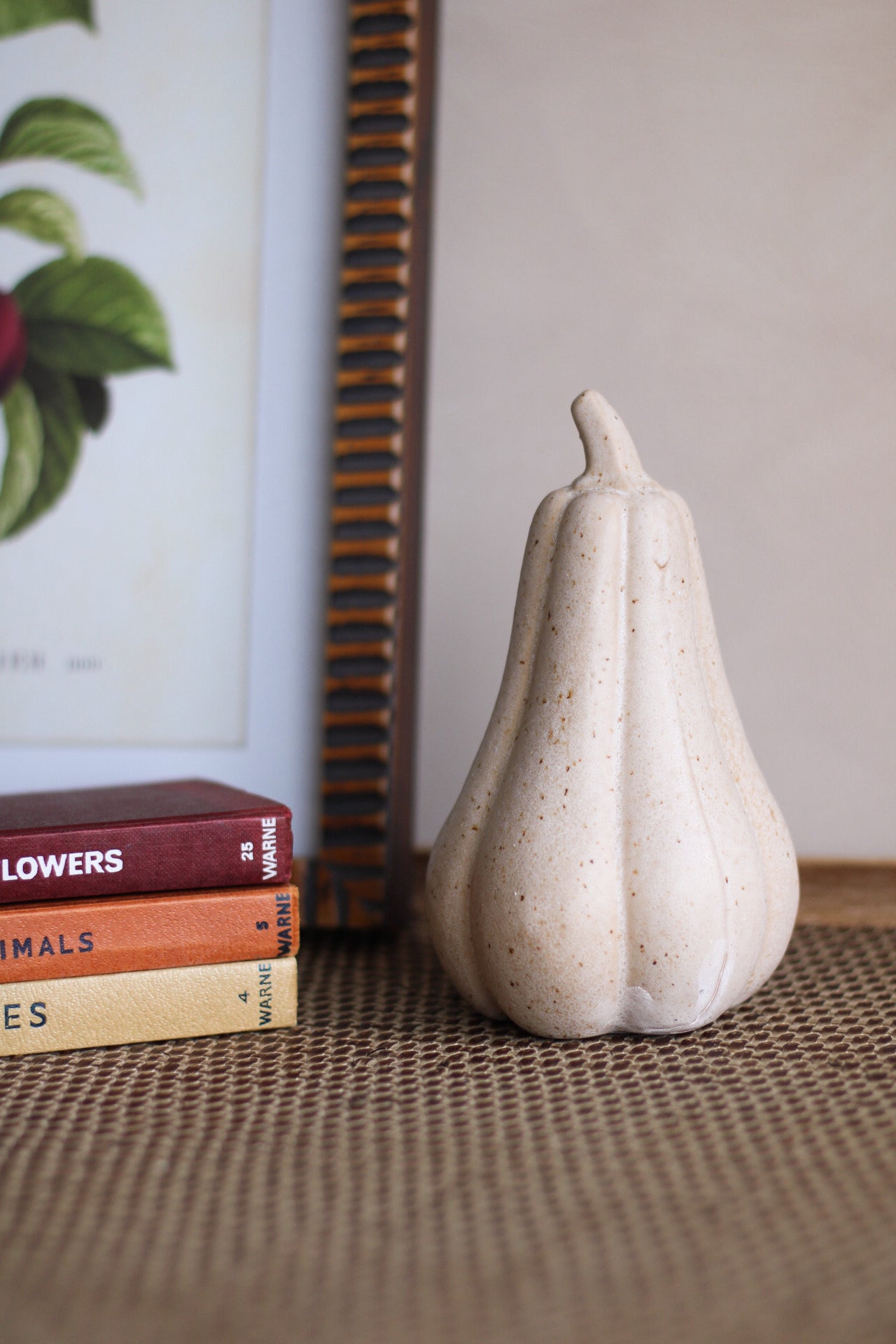 Decorative white gourd pumpkin object on a textured surface with books and a framed picture in the background.