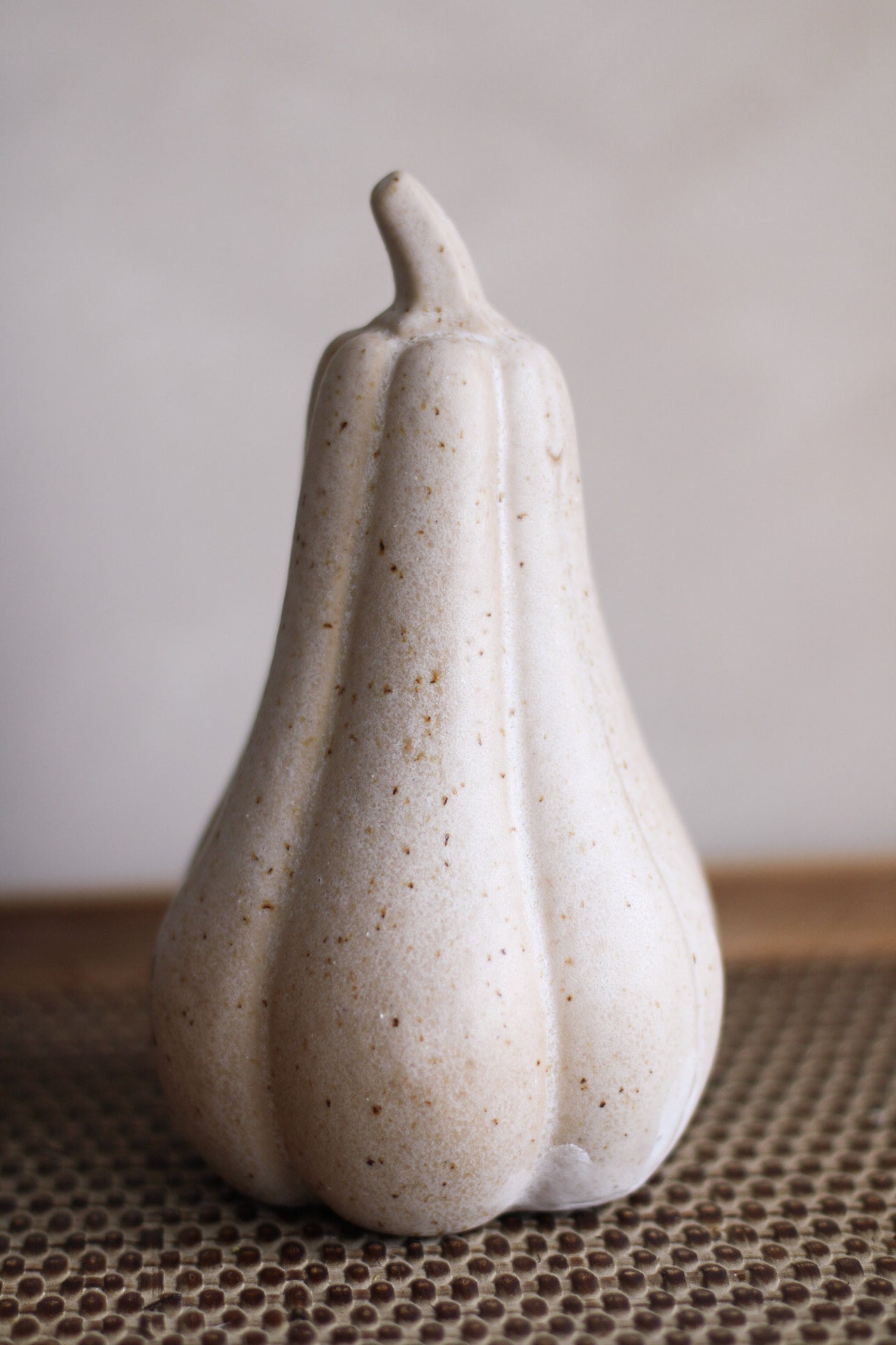 Speckled beige ceramic tall pumpkin shaped object on a textured surface with a neutral background