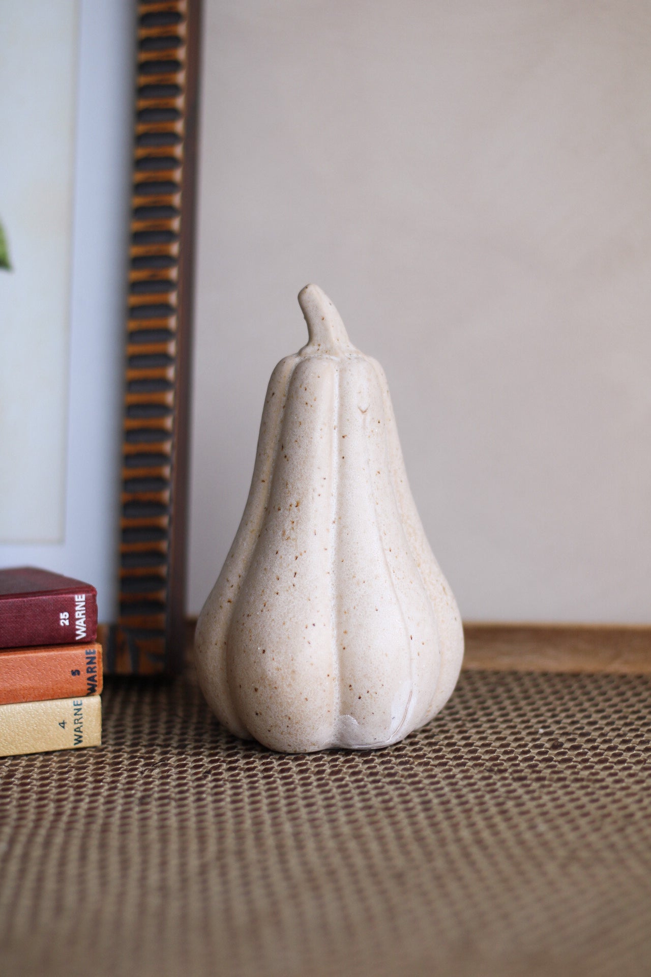 White ceramic pumpkin shaped object on a textured surface with books in the background