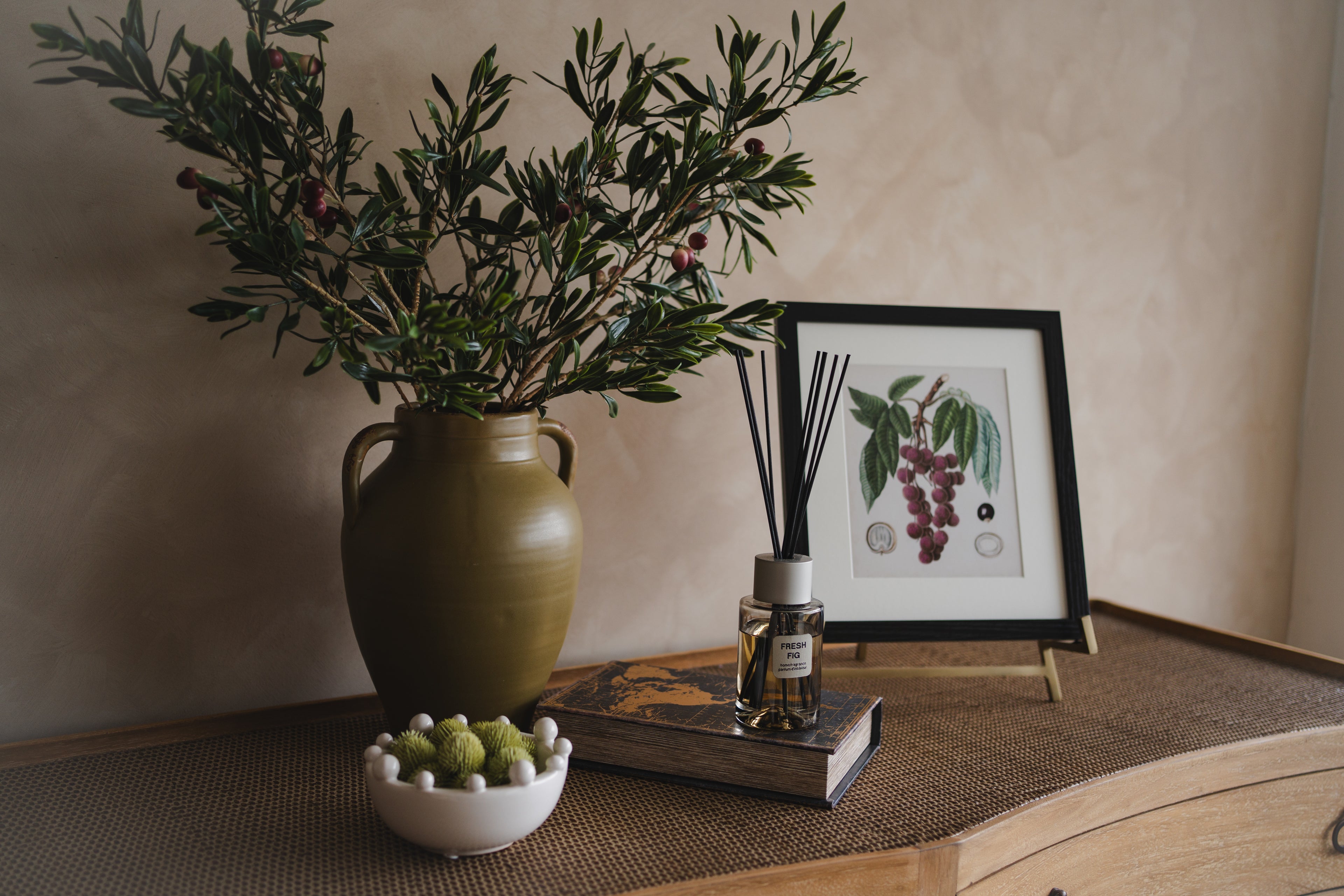 Decorative setup with a vase, plants, and a framed print on a wooden surface.