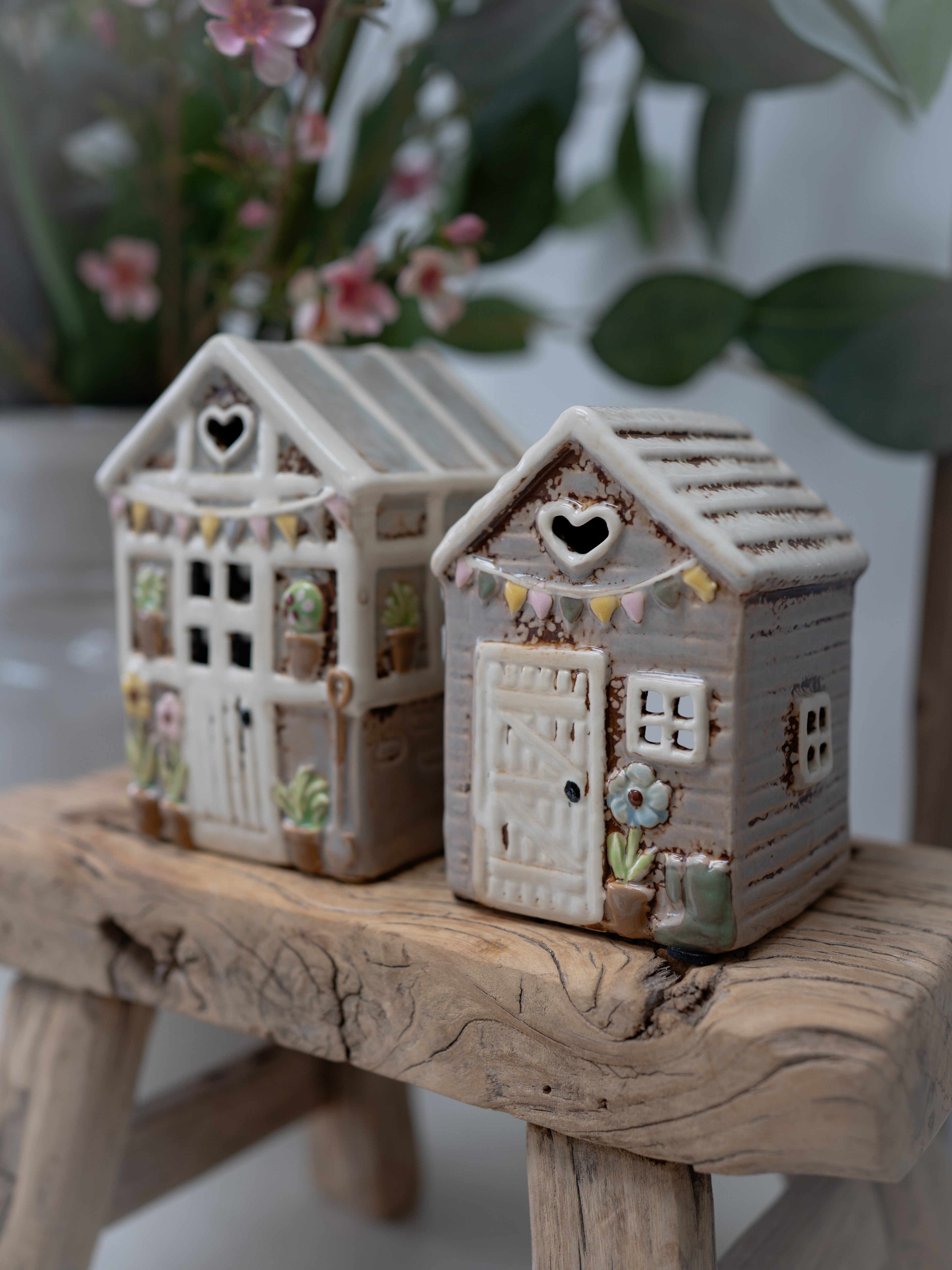 Two small ceramic houses on a wooden surface with a blurred floral background