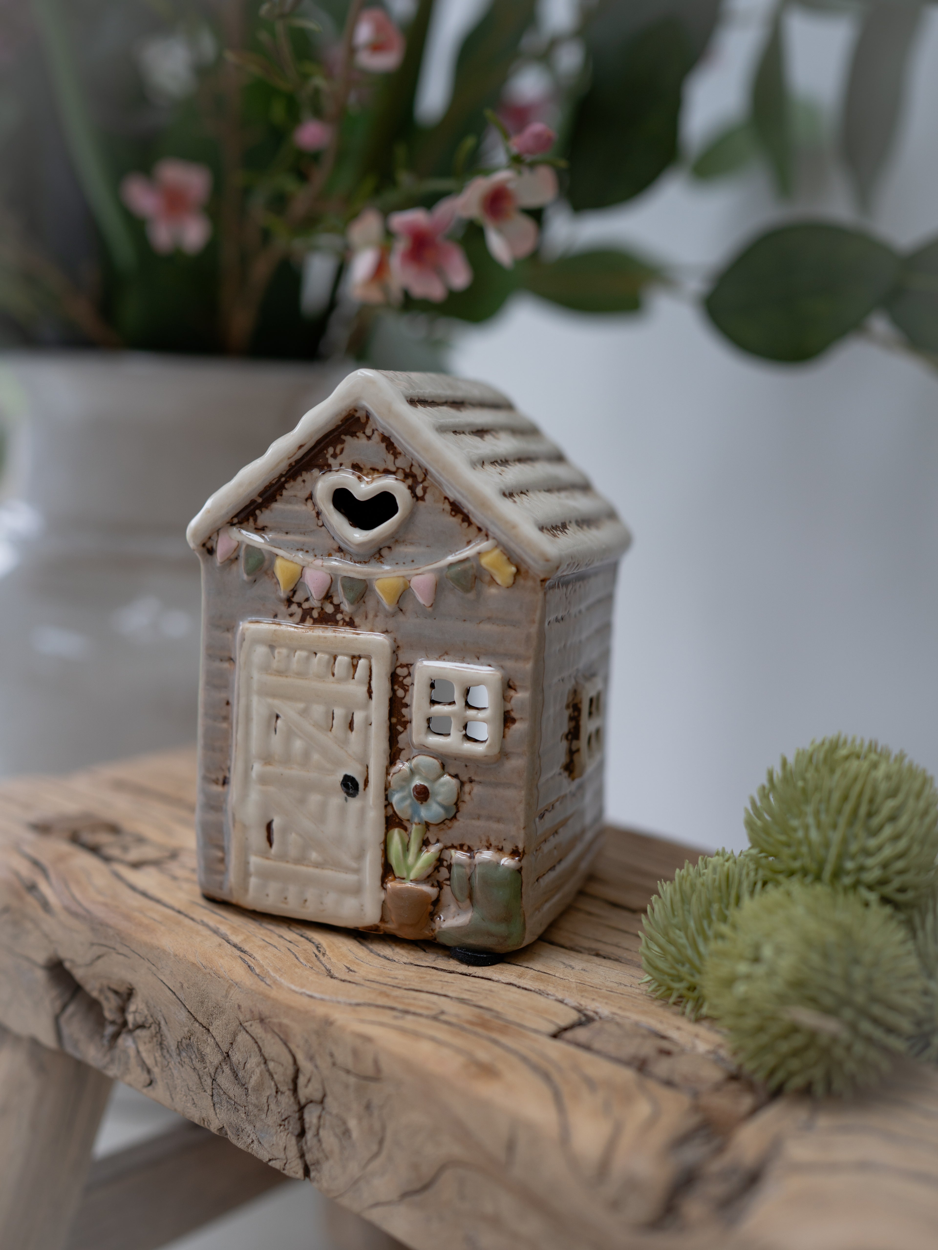 Small ceramic house on a wooden surface with plants in the background