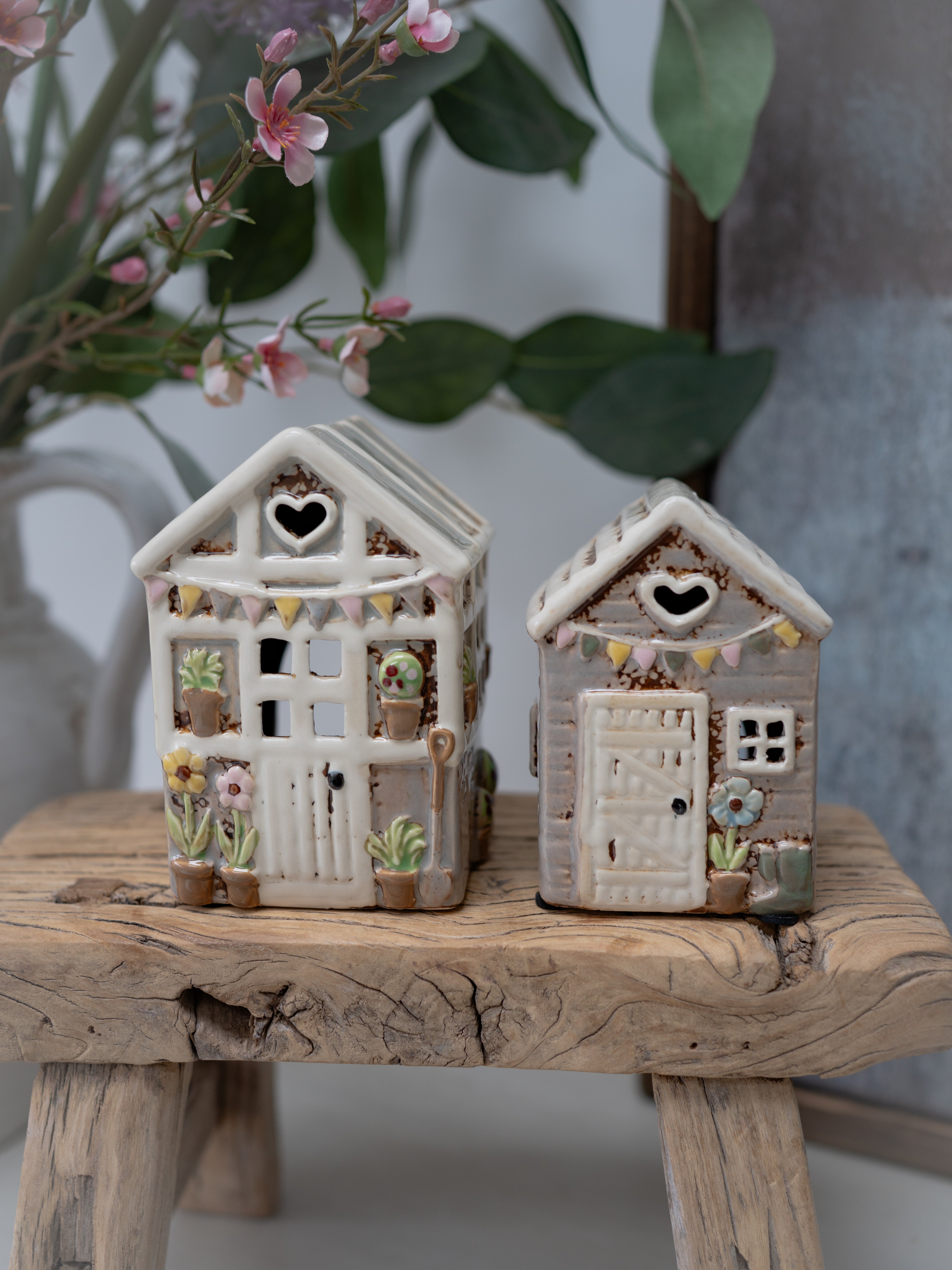 Two decorative ceramic houses on a wooden surface with a blurred floral background