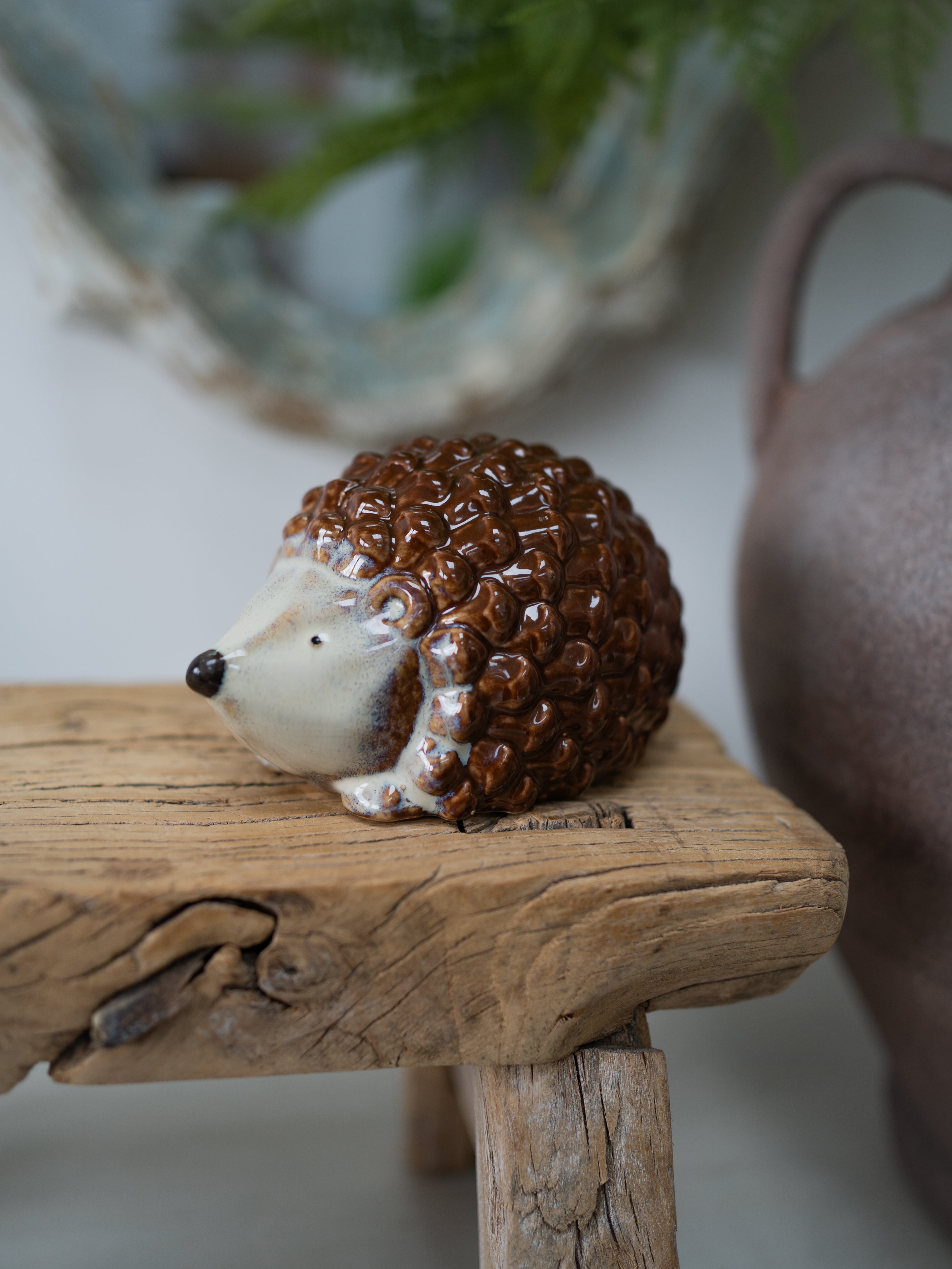 A small ceramic hedgehog figurine with brown textured spines and a cream-colored face, resting on a rustic wooden block.