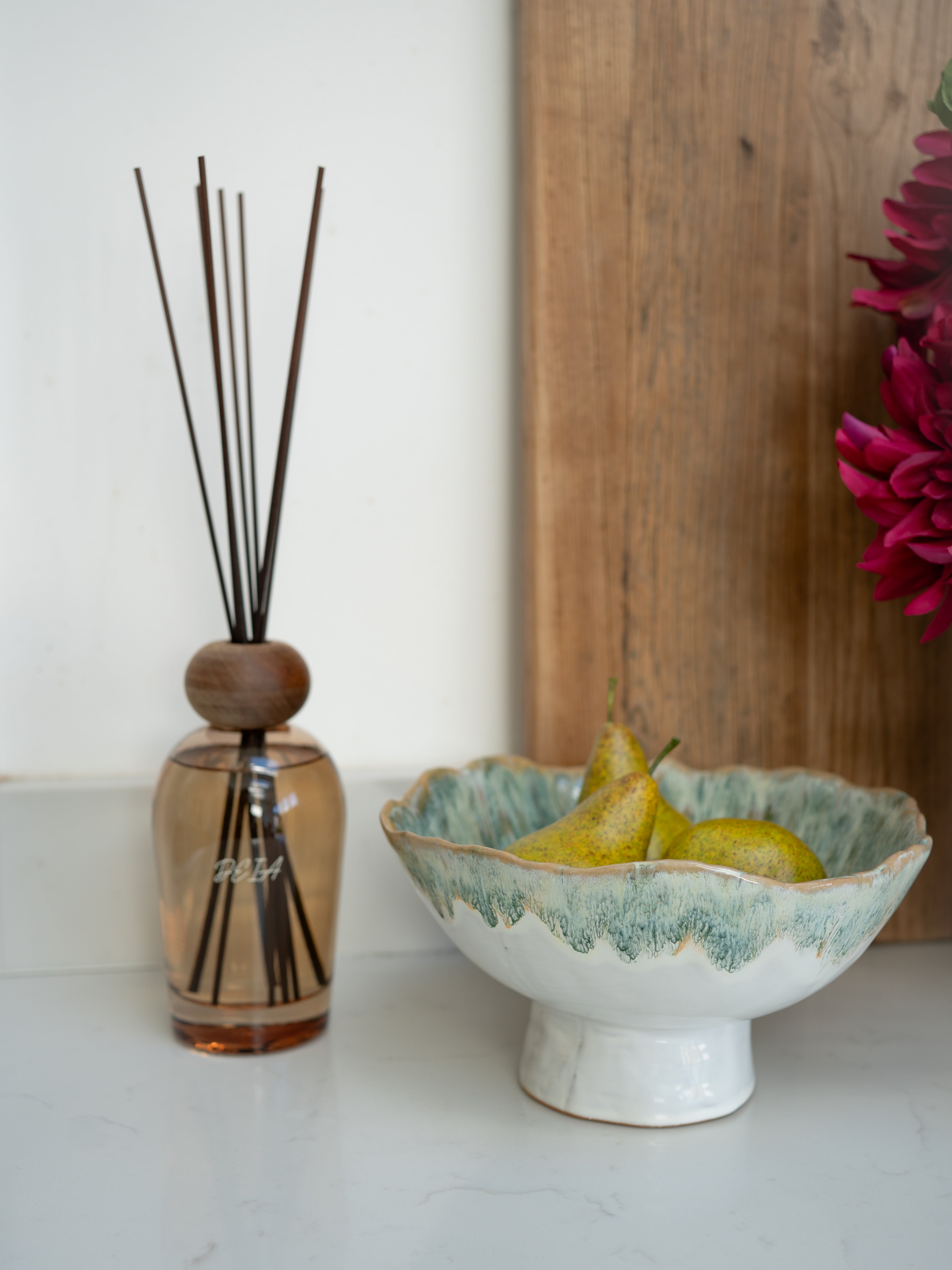Decorative bowl with pears next to a luxury reed diffuser on a white surface