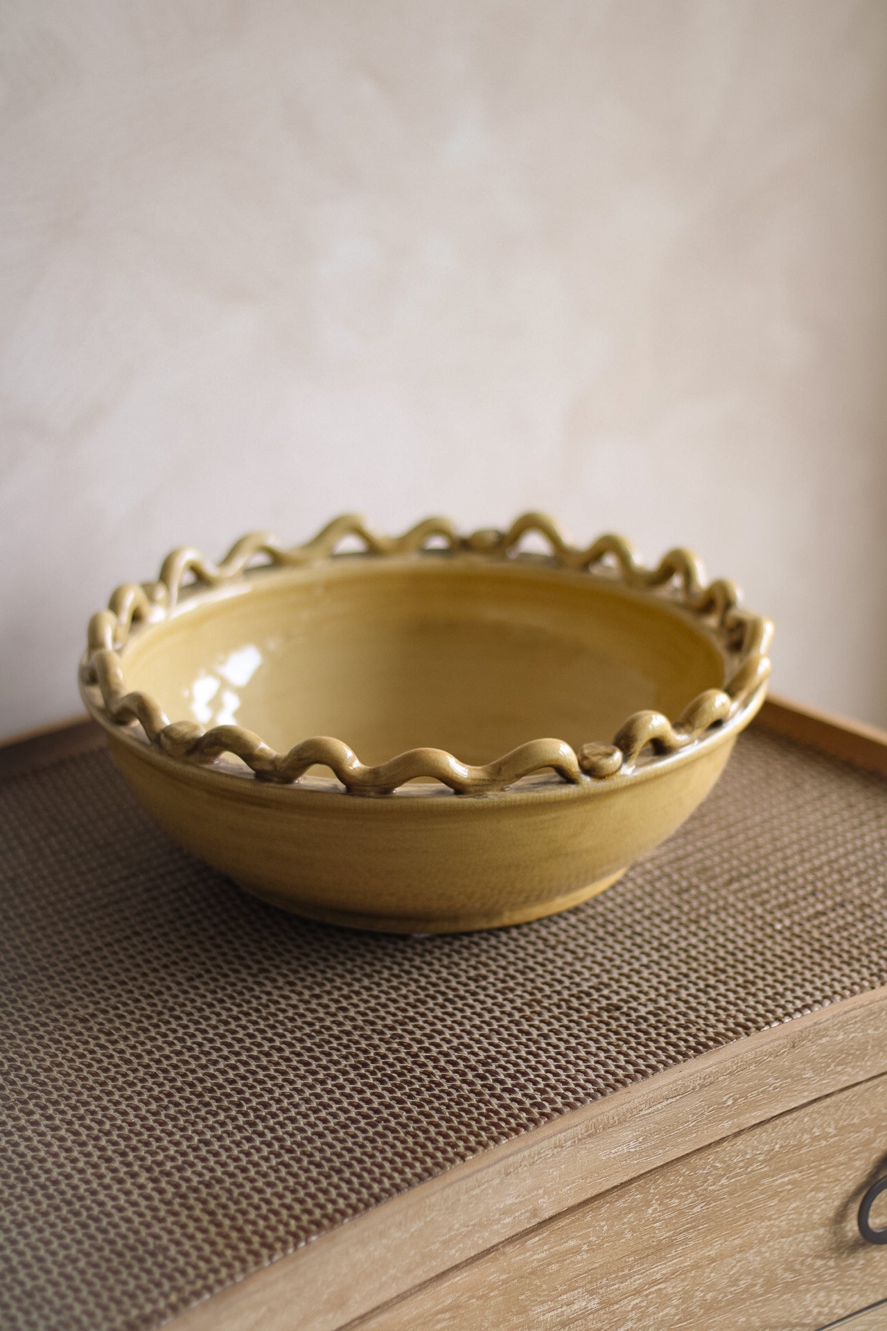 Yellow ceramic fruit bowl with decorative edge on a textured surface