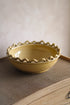 Yellow ceramic fruit bowl with decorative edge on a textured surface