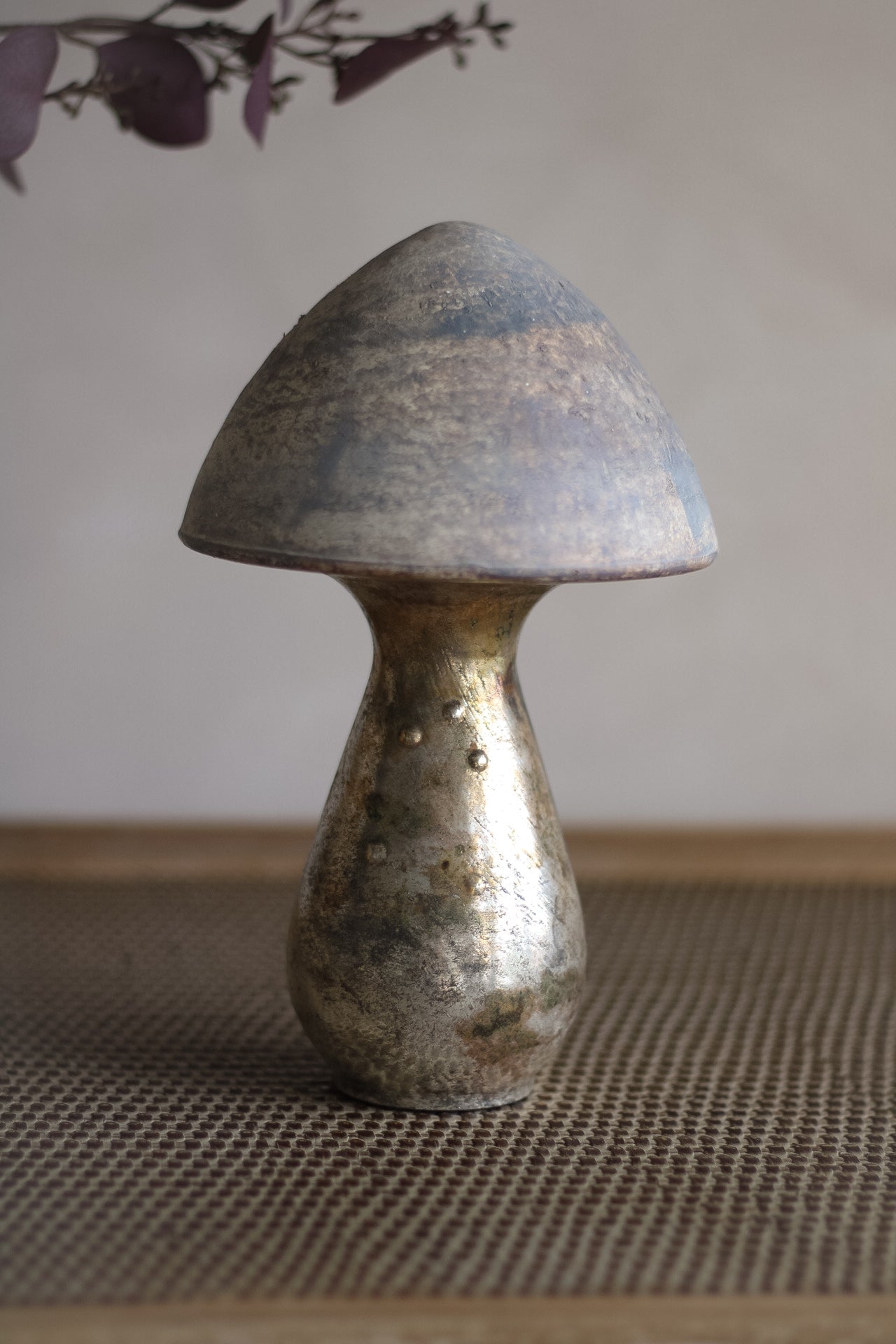 Decorative copper mushroom sculpture on a textured surface with a neutral background
