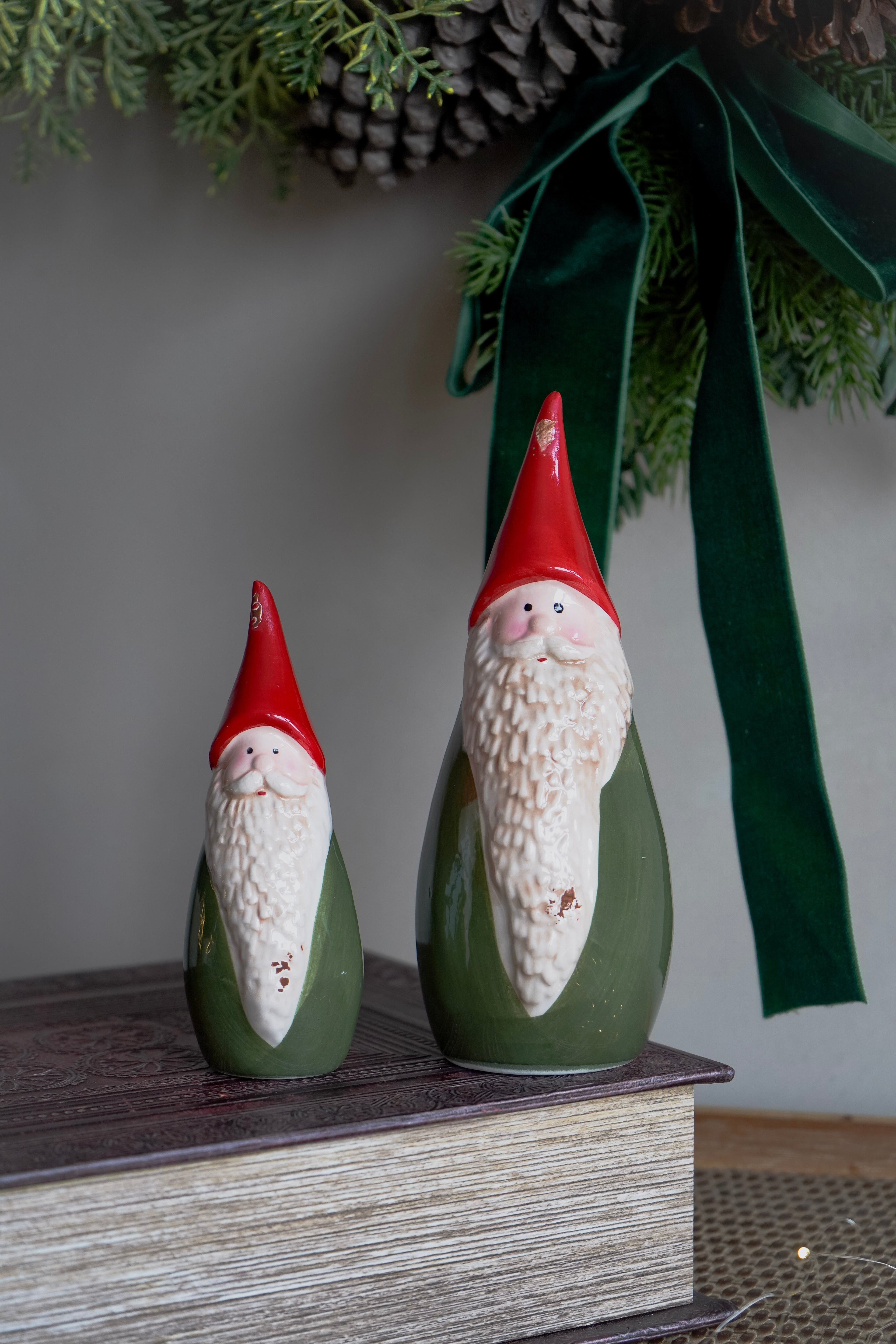 Two ceramic gnomes with red hats and green bodies on a wooden surface with a blurred background.