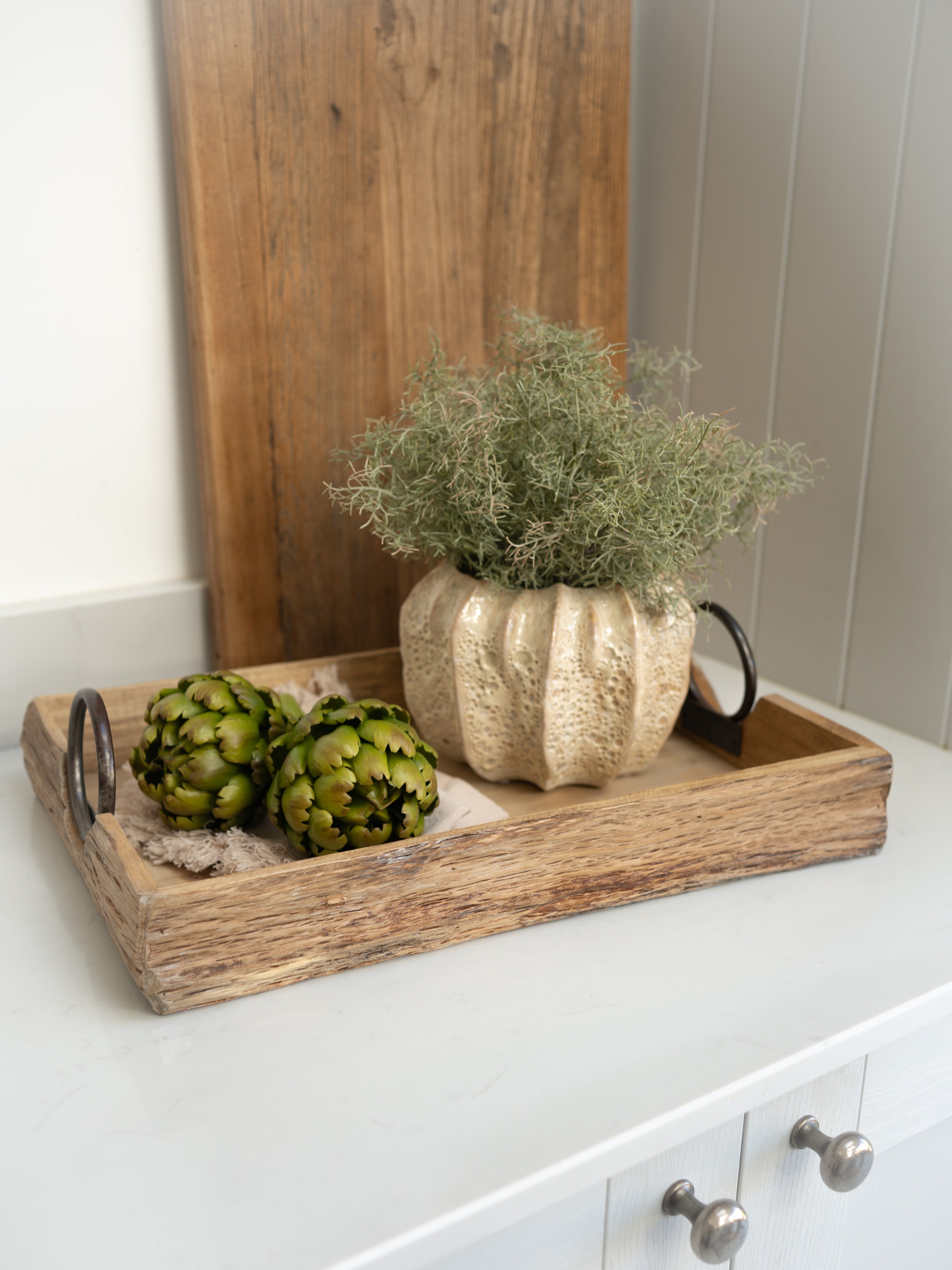Decorative tray with artichokes and a decorative plant pot with faux spanish moss on a white surface.