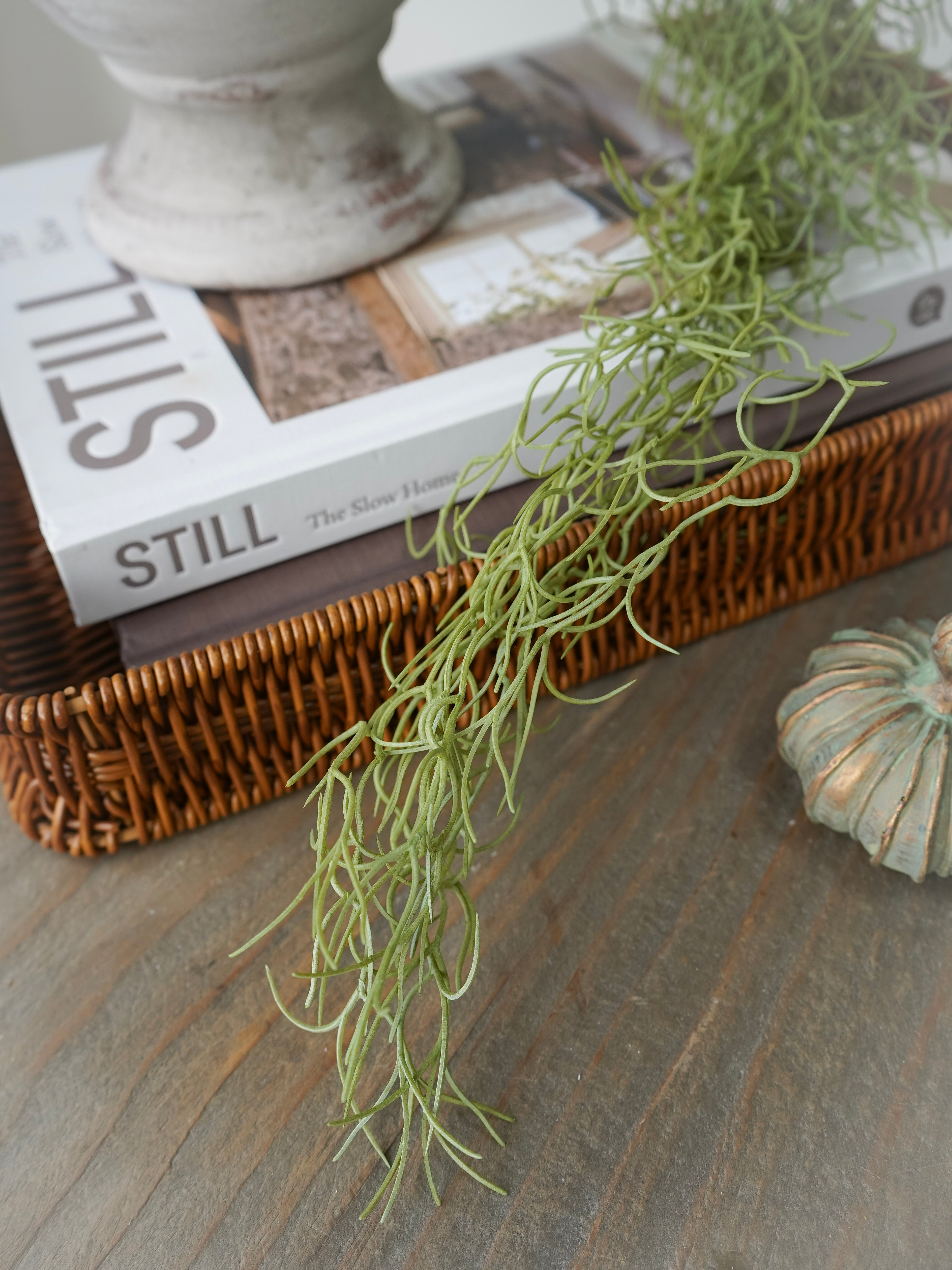 Decorative greenery on a surface with a book and wicker basket in the background