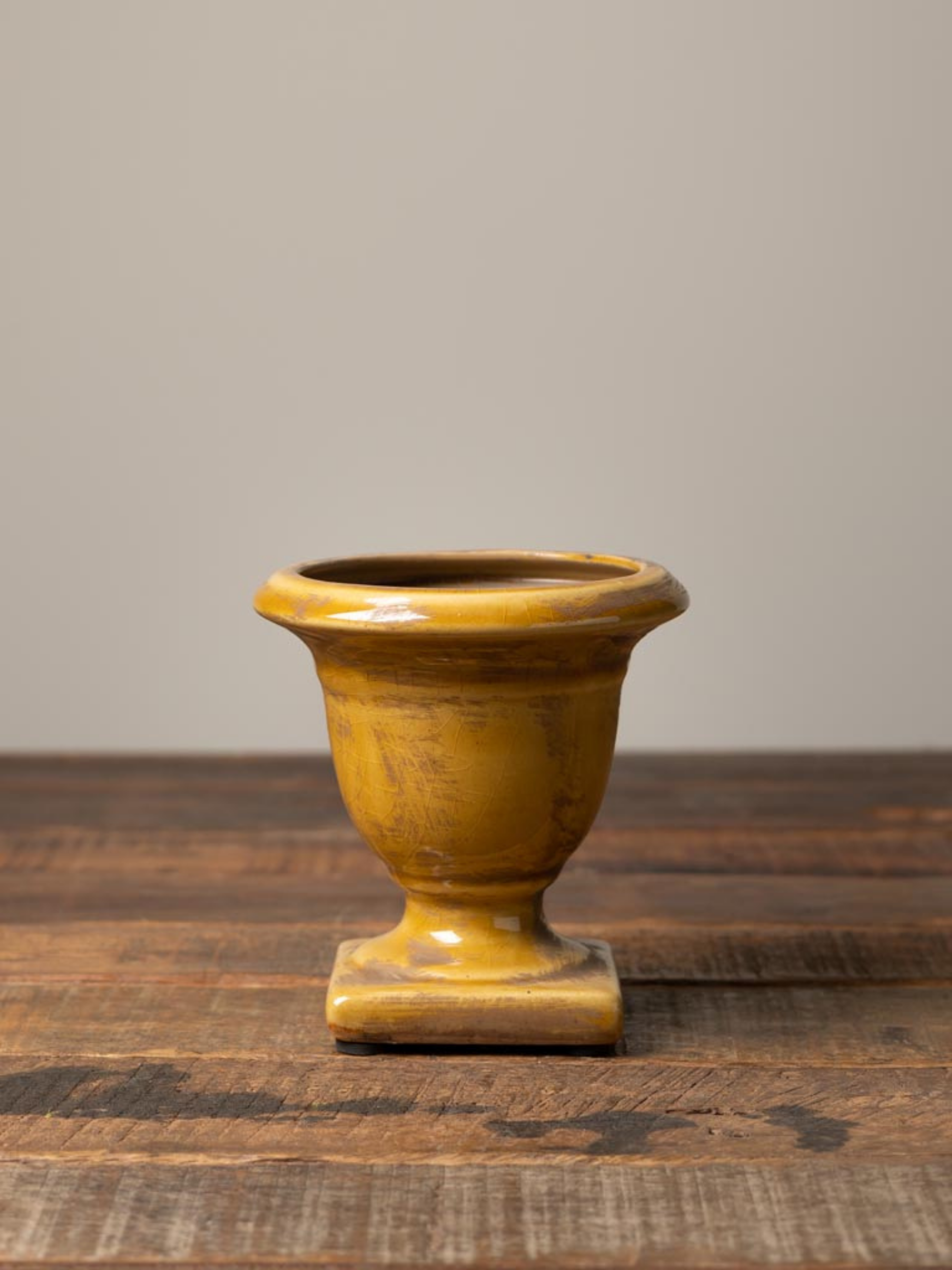 mustard ceramic urn on a wooden surface with a gray background