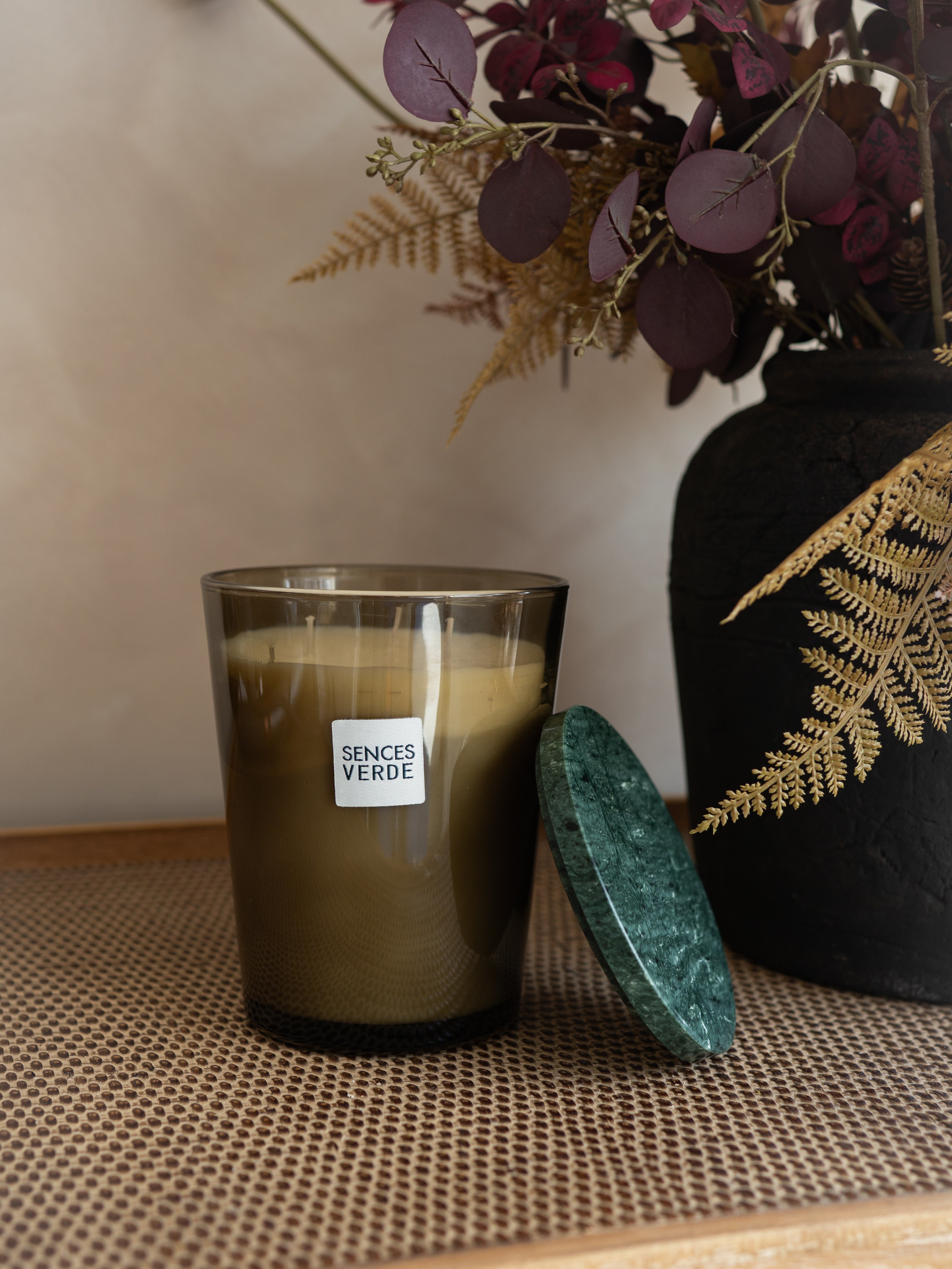 A candle in a dark amber glass jar with a white label reading &