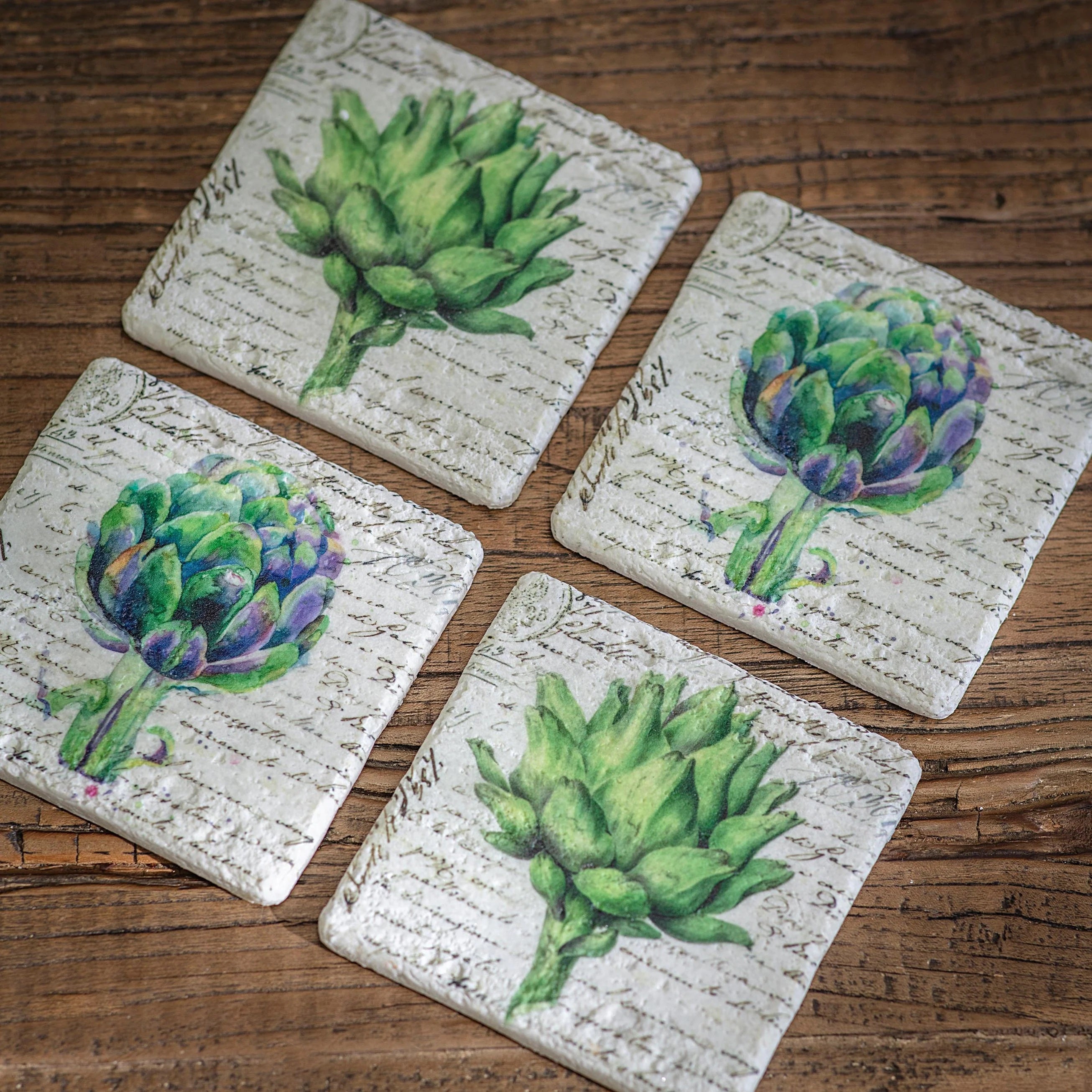 Four coasters with artichoke design on a wooden surface