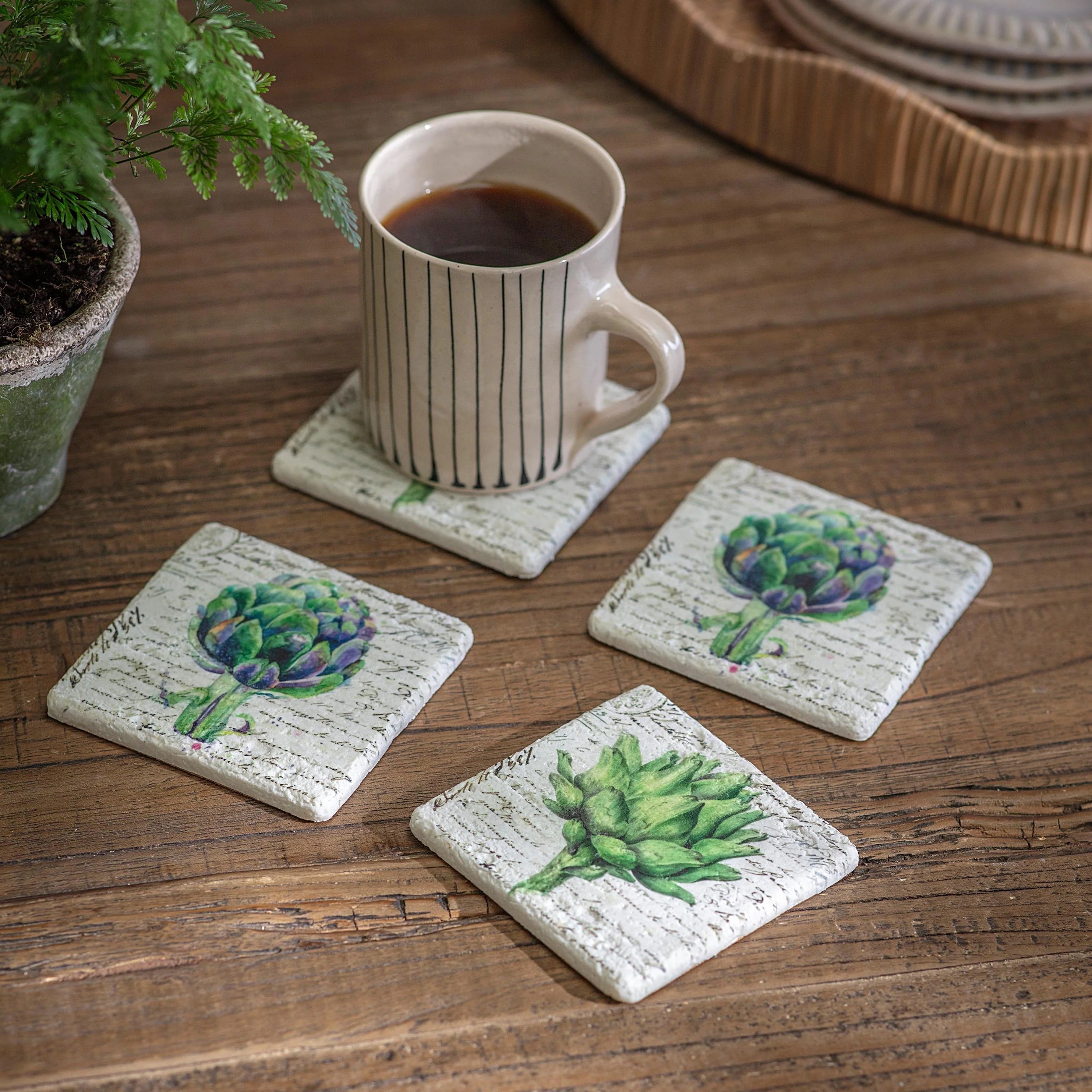Set of four decorative coasters with plant designs on a wooden surface with a mug of coffee.