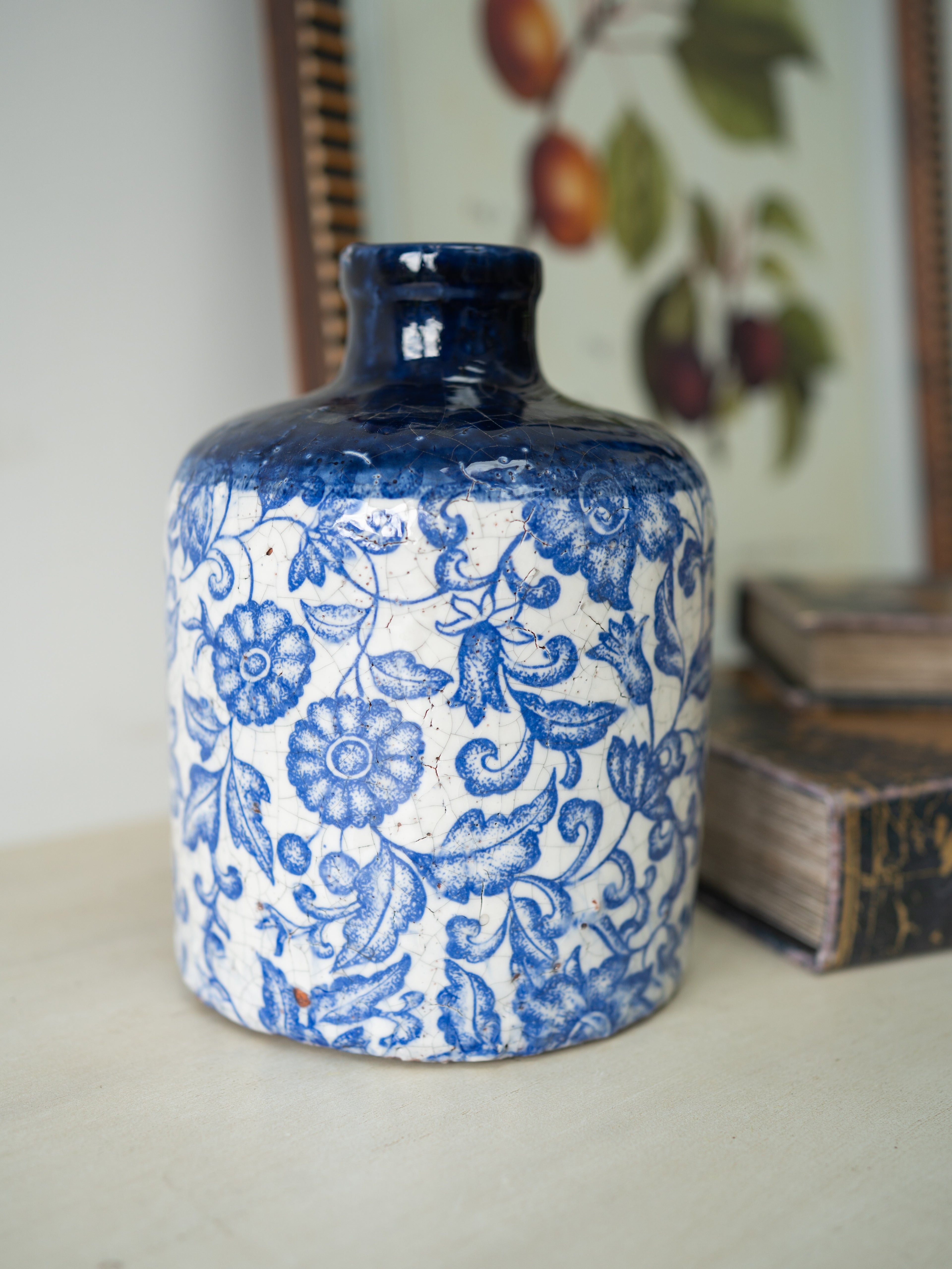 Blue and white patterned ceramic jar on a surface with a framed artwork in the background.