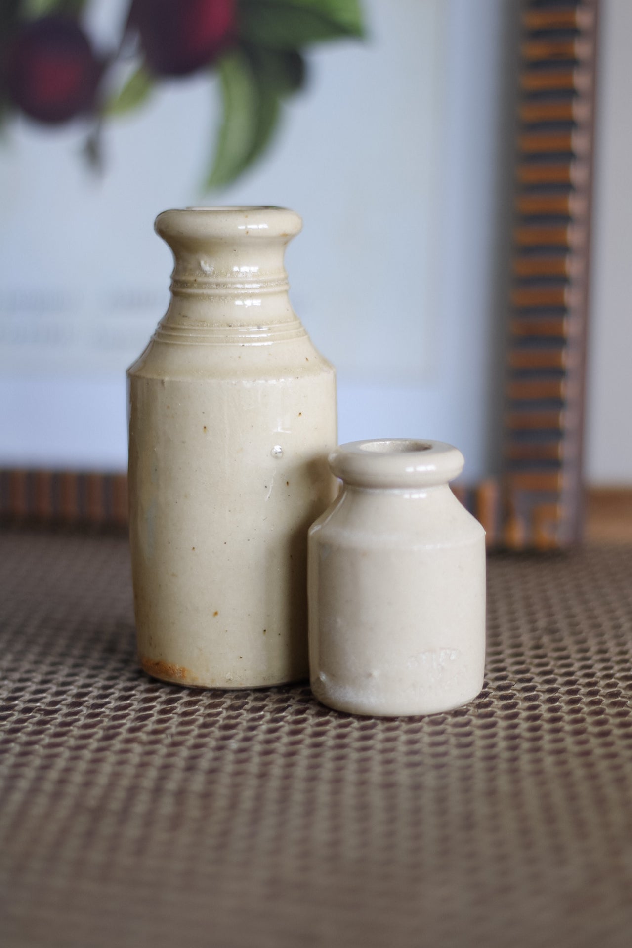 Two cream vintage ink bottles on a textured surface with a blurred background