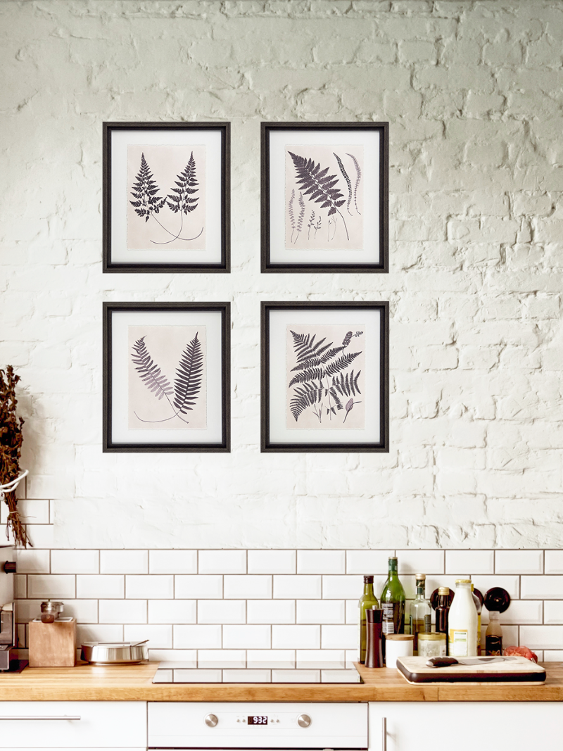 Four framed leaf prints on a white brick wall above a kitchen counter.