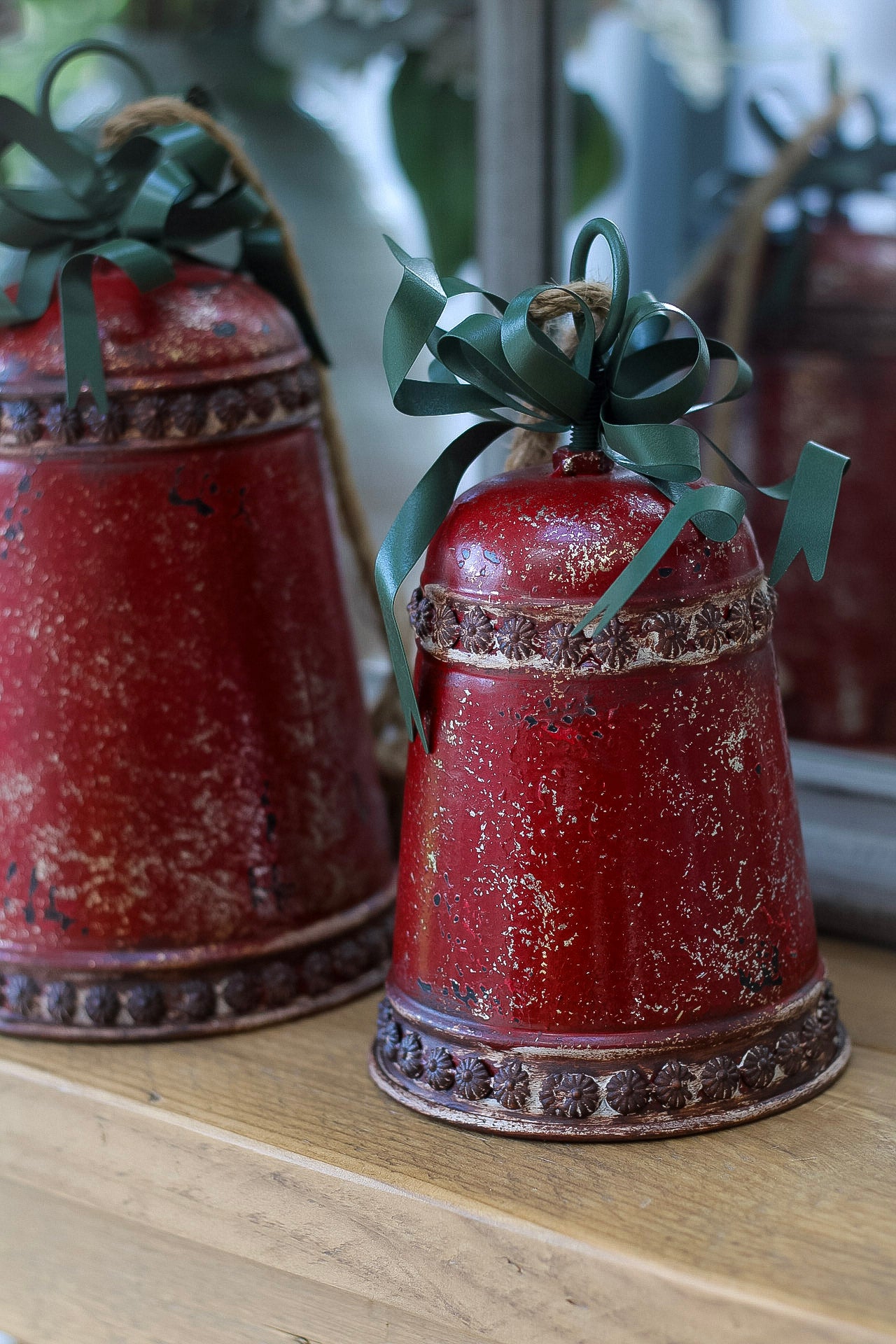 Two rustic red bells with green ribbons on a wooden surface.