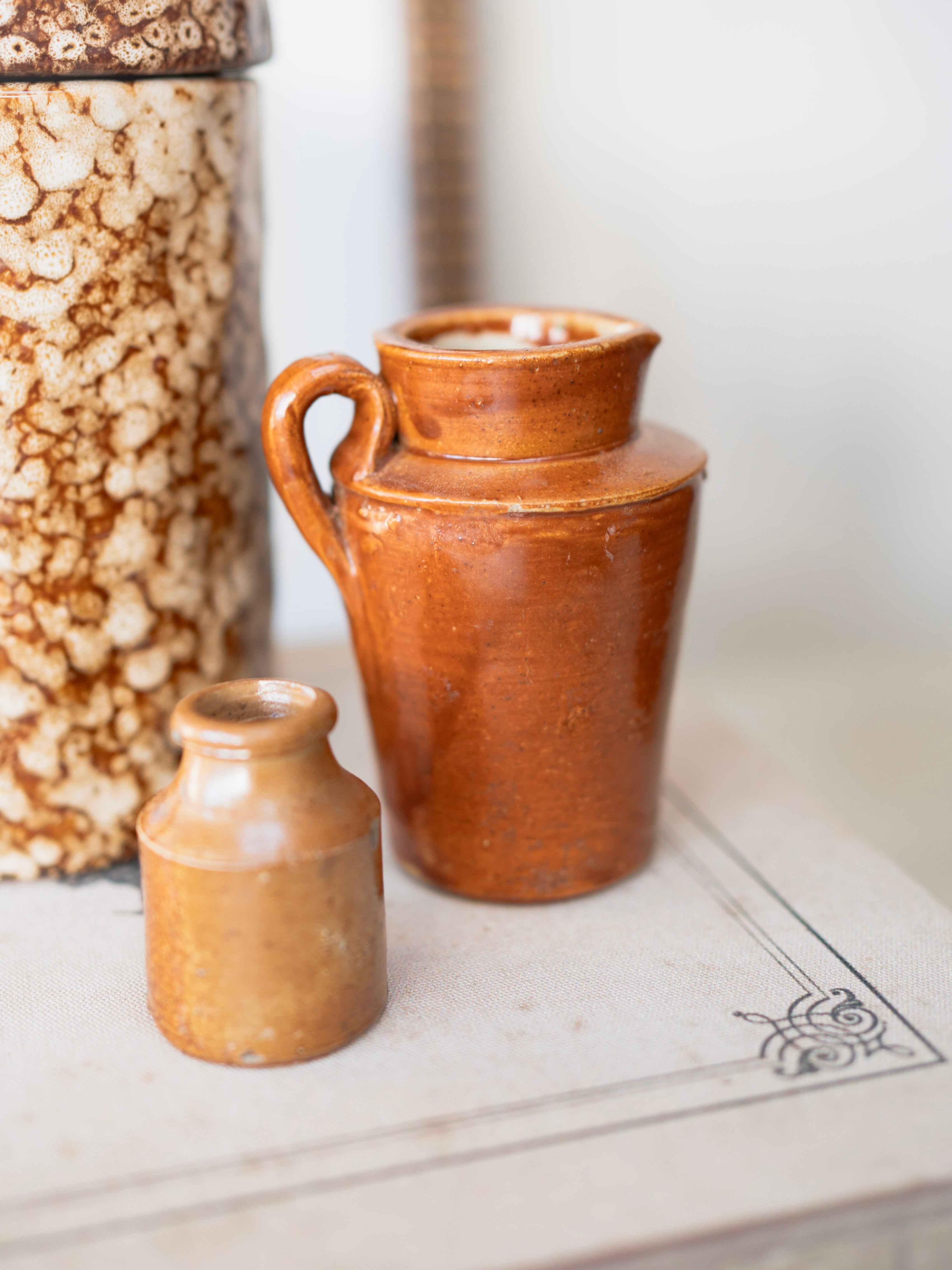 Two brown ceramic vintage jugs on a white surface with a blurred background