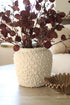 Decorative vase with textured barnacle surface holding a plant on a table.