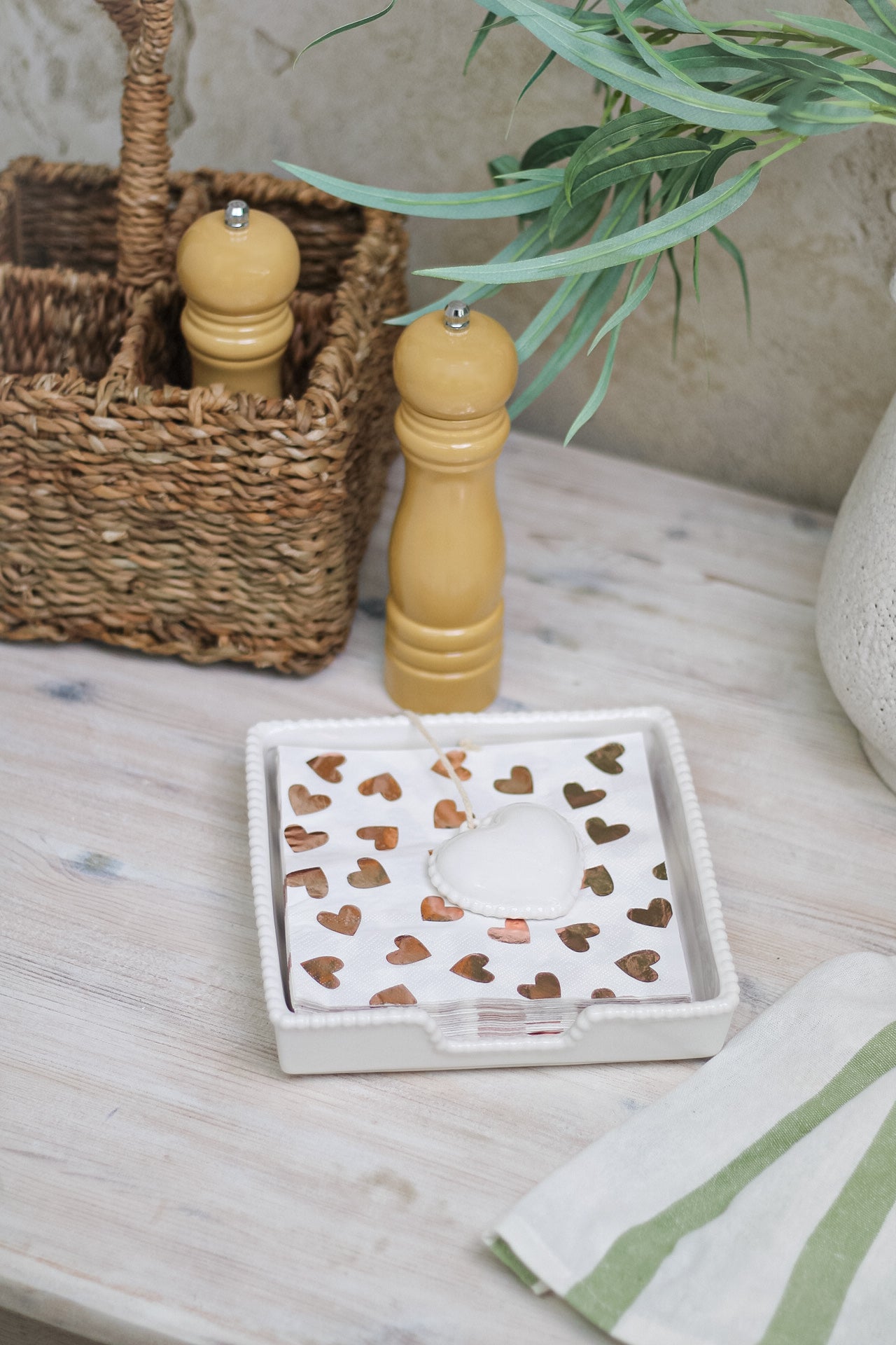 A white ceramic napkin tray with a beaded edge and heart pattern in the center, displayed on a table with a salt shaker and pepper grinder in the background.
