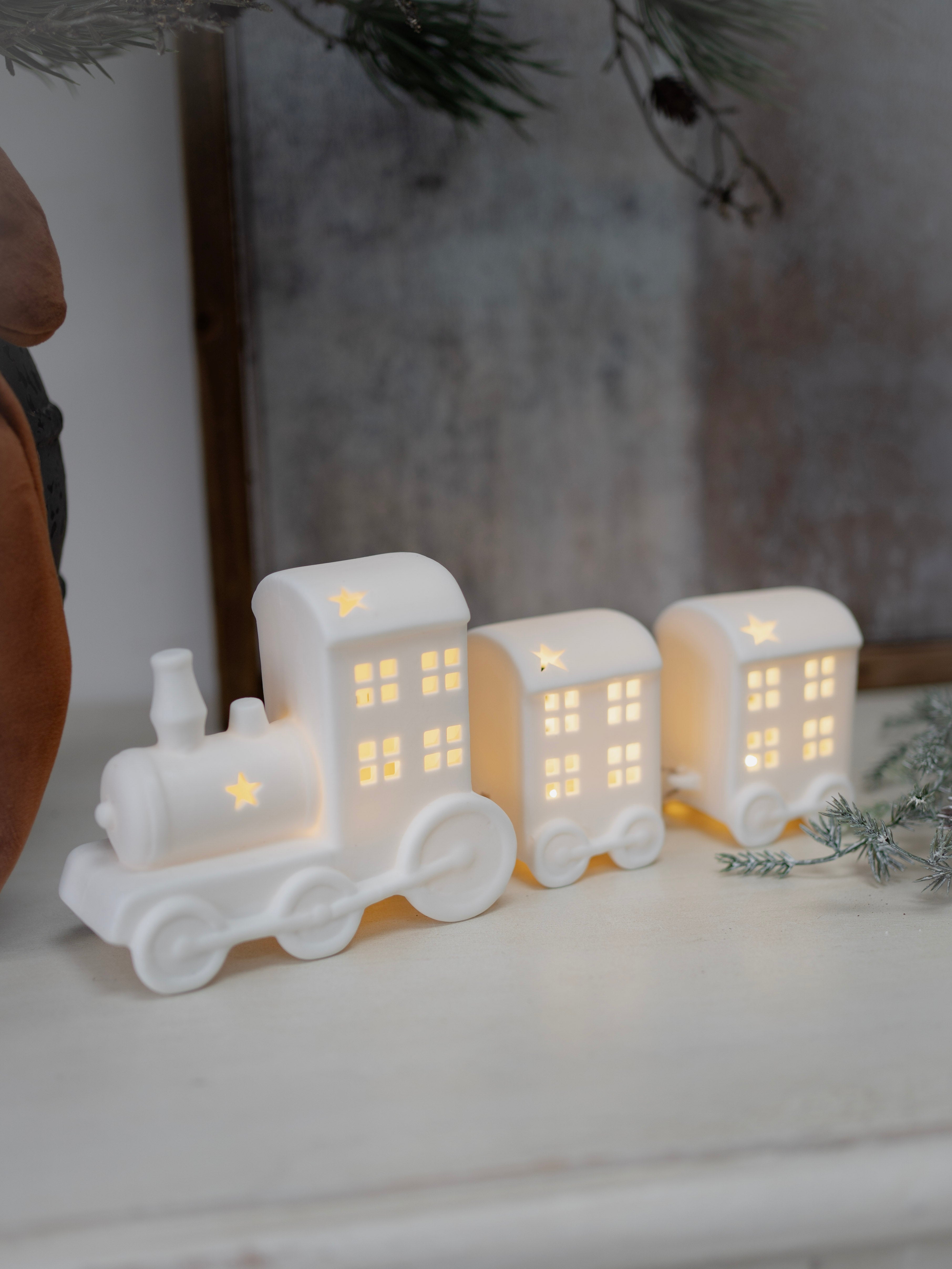 White ceramic train decoration with lit-up windows on a white surface.