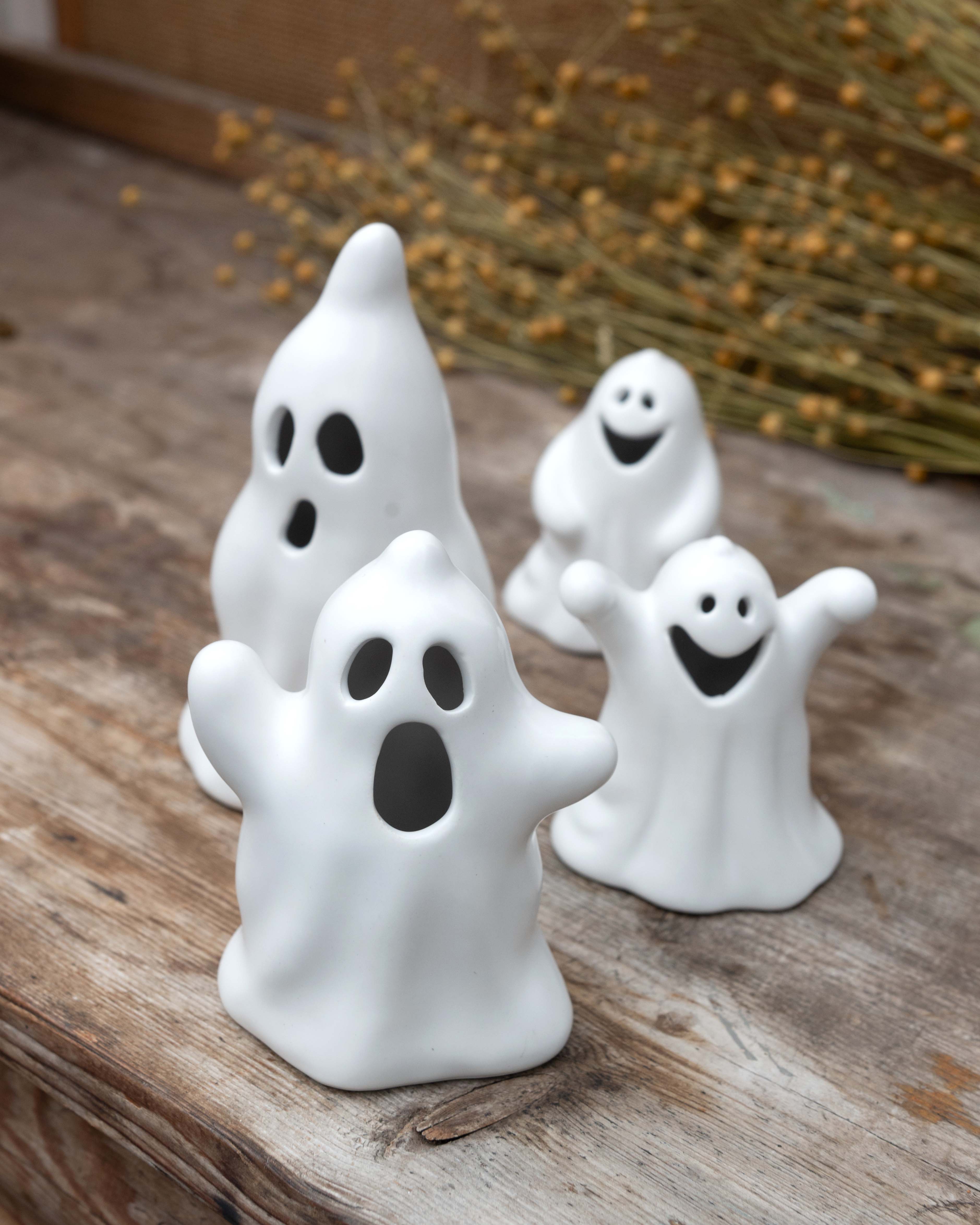 Set of white ghost figurines on a wooden surface with dried plants in the background