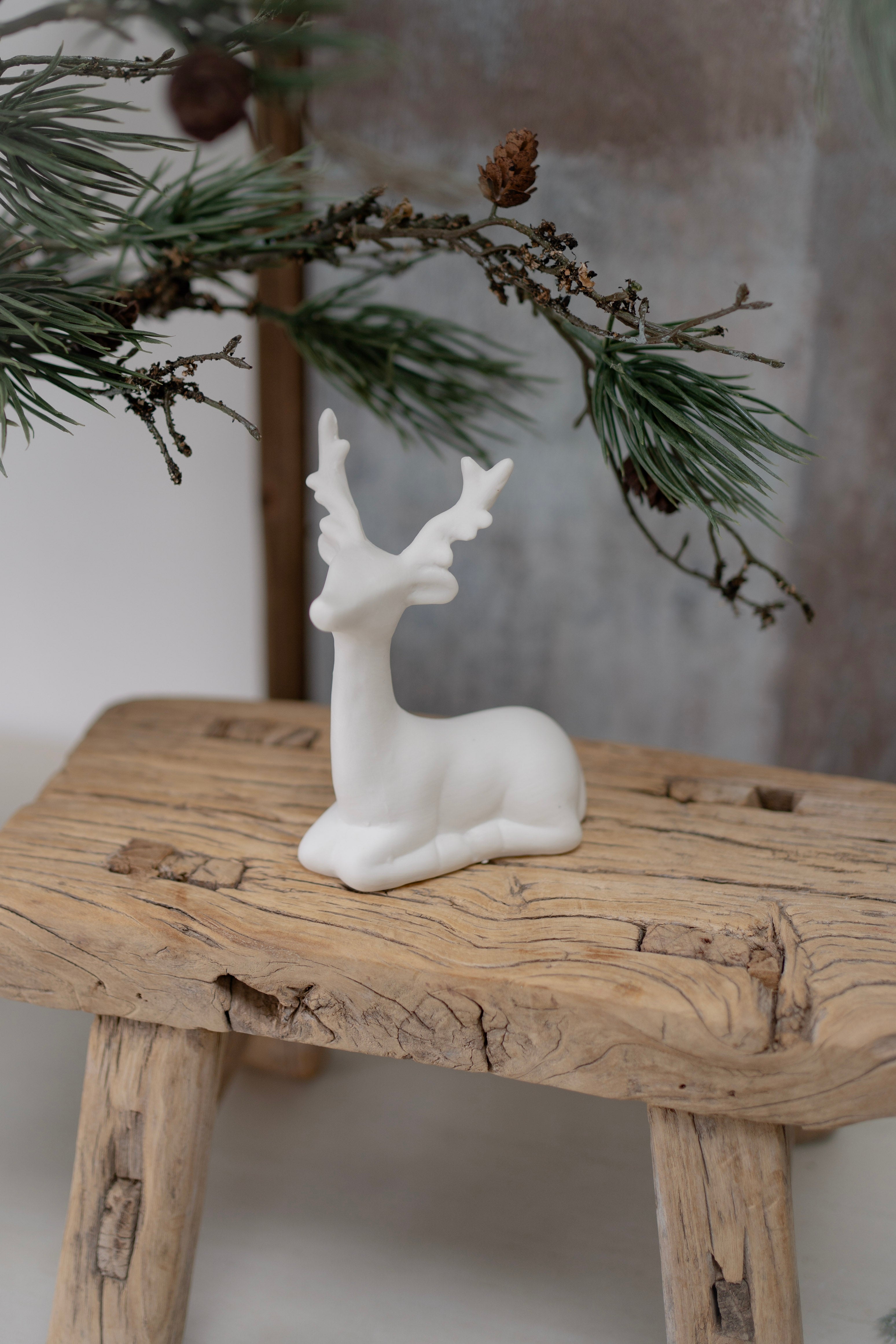 White deer figurine on a wooden surface with greenery in the background