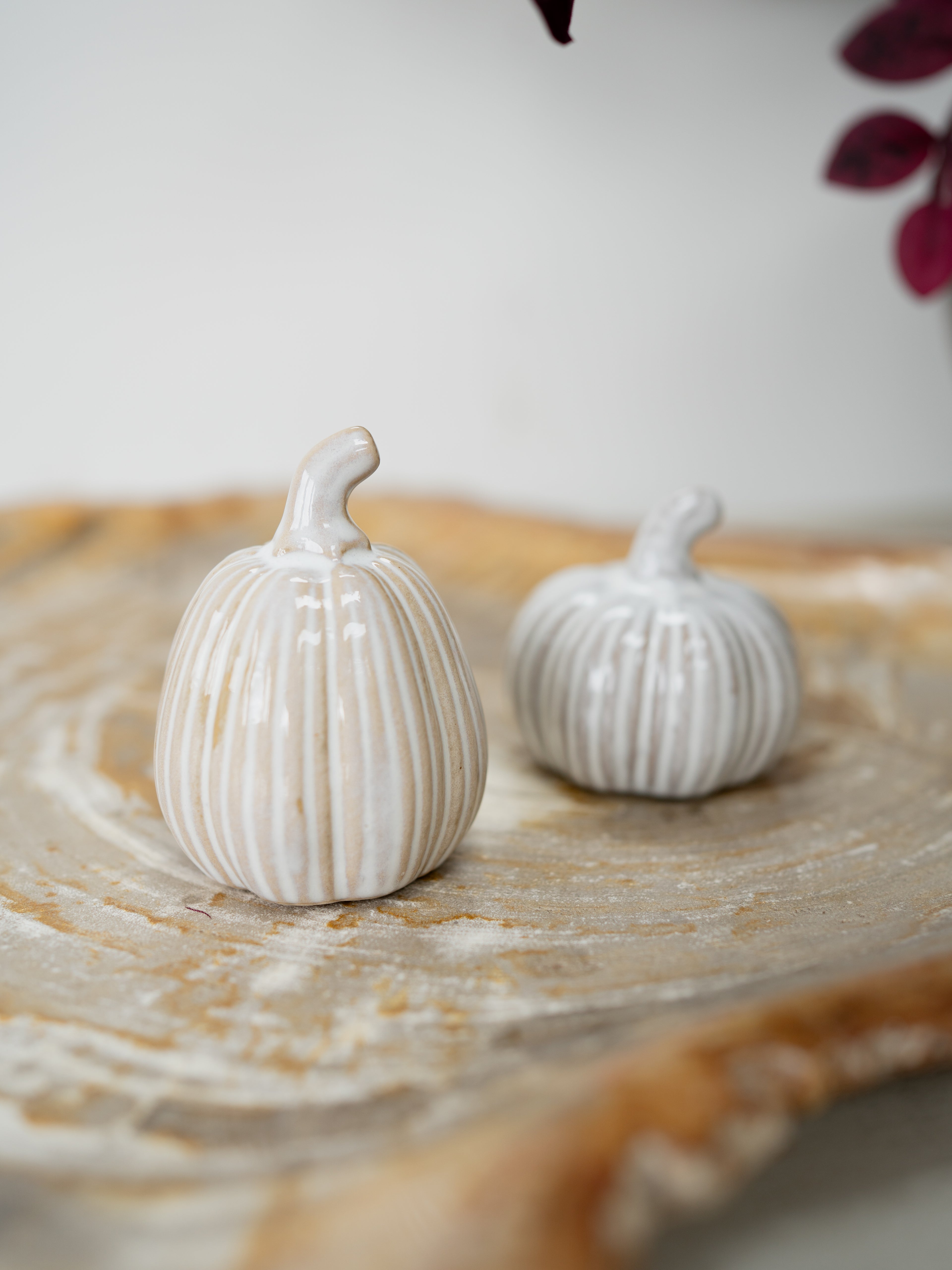 Two small ribbed decorative pumpkins in an off-white glazed ceramic finish, displayed on a round wooden slice tray.