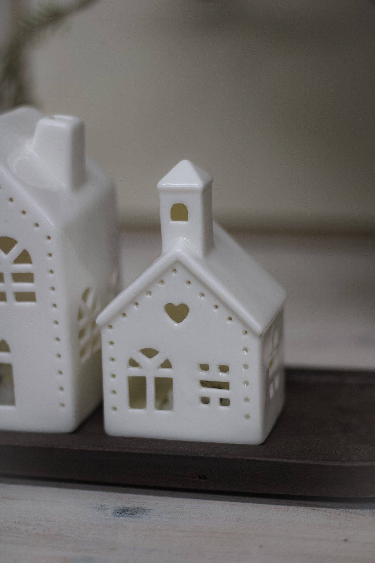 White ceramic houses with cut-out hearts and dots design, illuminated from the inside by LED lights, placed on a wooden surface.
