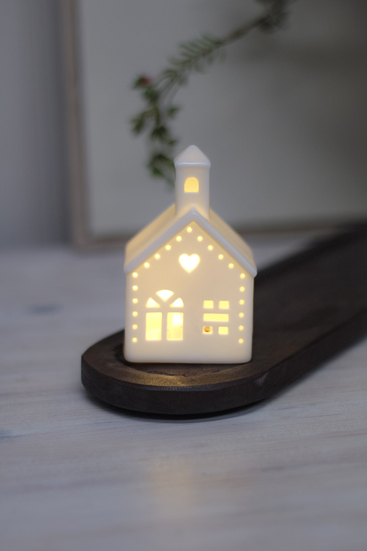 White ceramic houses with cut-out hearts and dots design, illuminated from the inside by LED lights, placed on a wooden surface.