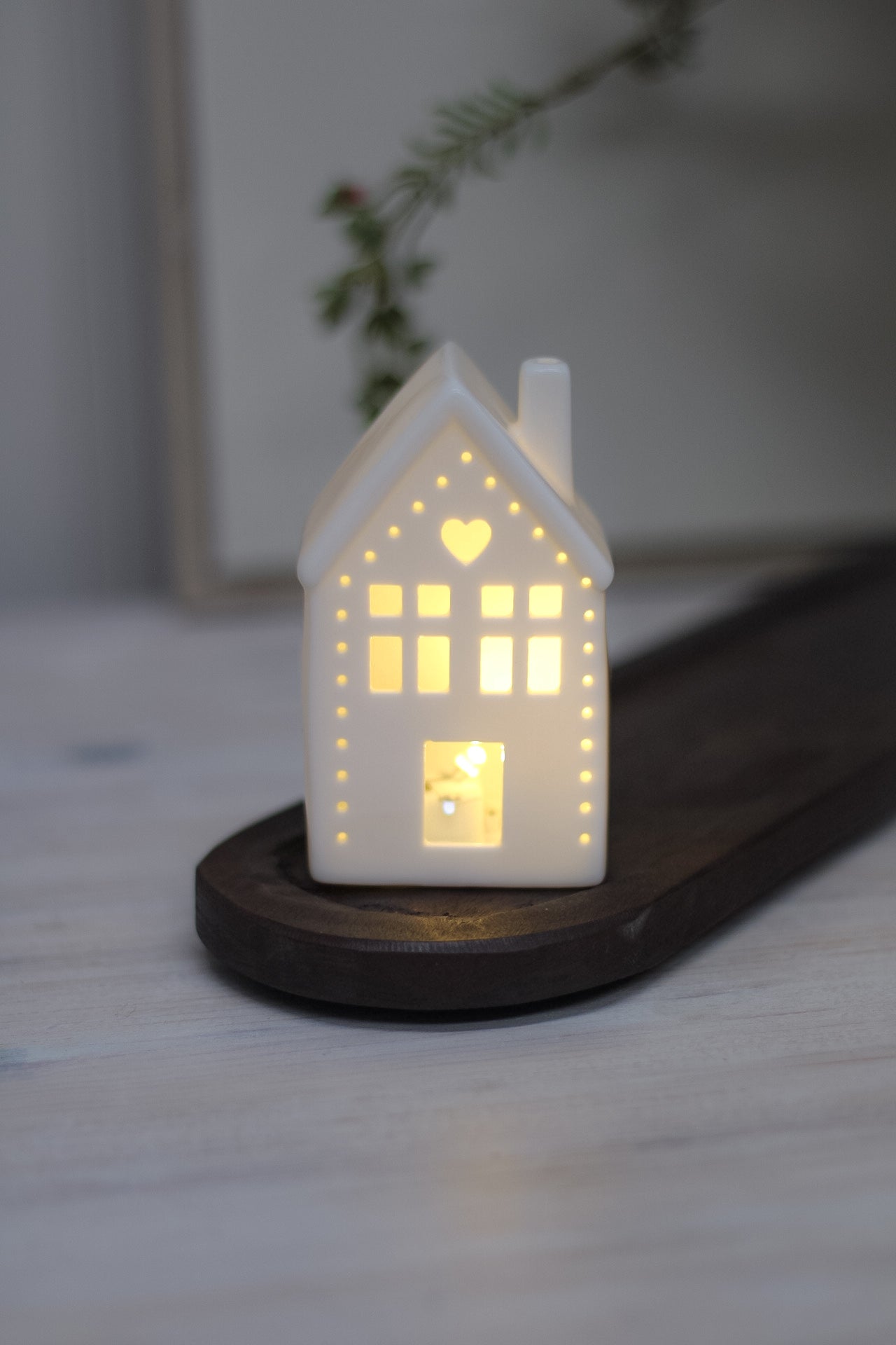 White ceramic houses with cut-out hearts and dots design, illuminated from the inside by LED lights, placed on a wooden surface.