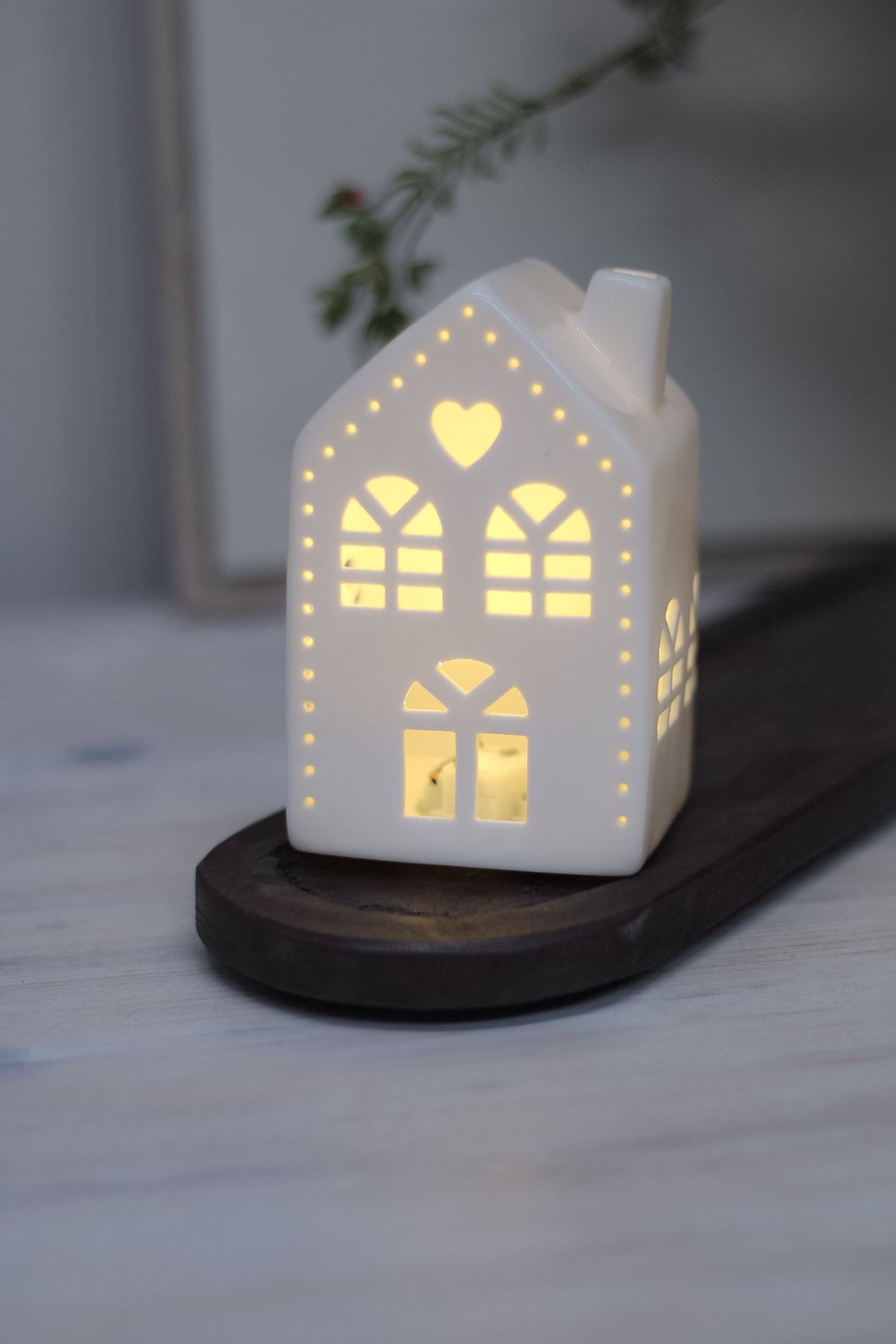 White ceramic houses with cut-out hearts and dots design, illuminated from the inside by LED lights, placed on a wooden surface.