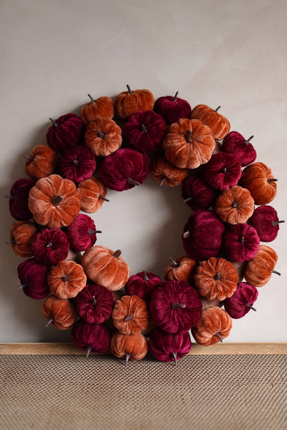 Decorative wreath with orange and red pumpkins on a neutral background