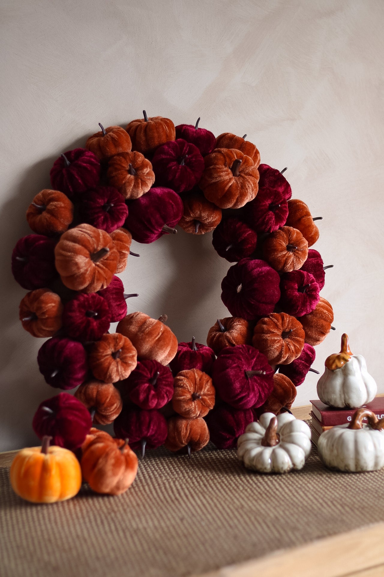 Decorative wreath made of pumpkins in red, orange, and white on a neutral background.