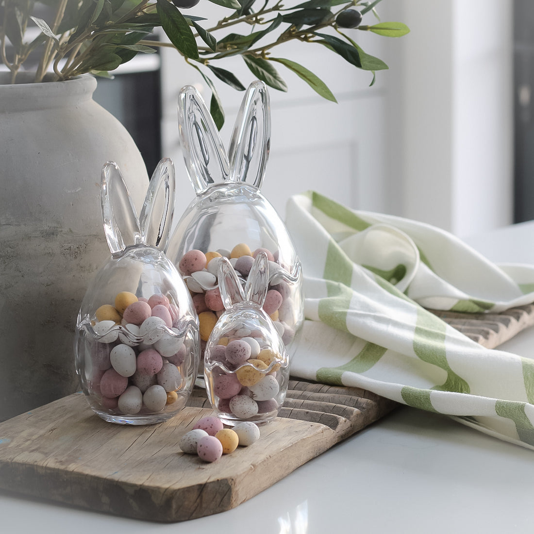 Glass bunny ears jars, filled with mini eggs on top of wooden board