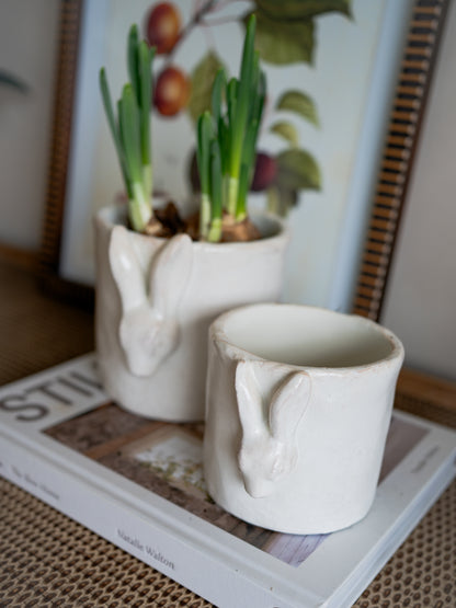 Two ceramic rabbit-shaped planters with small plants on a book