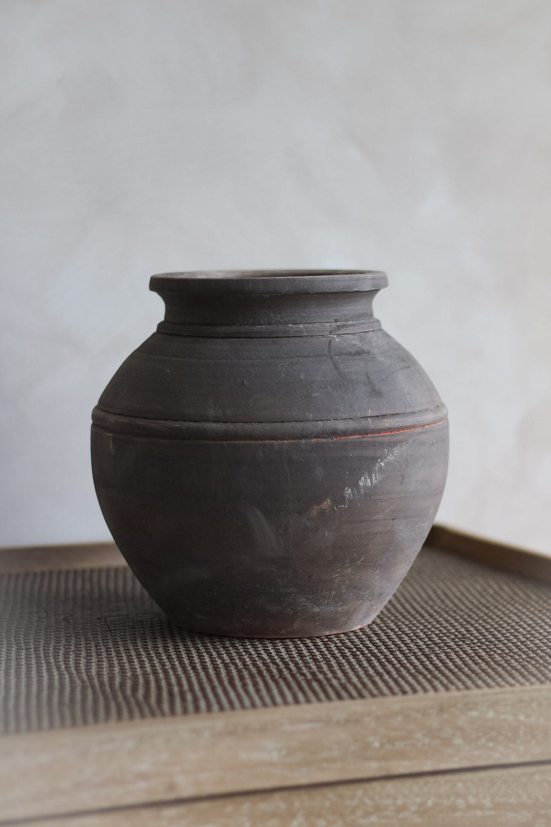 Earth brown clay pot on a textured surface with a neutral background