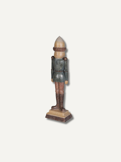 A vintage wooden nutcracker figurine standing on a rectangular base, featuring a pointed beige hat, a dark green jacket, brown pants, and a matching base, set against a plain off-white background.