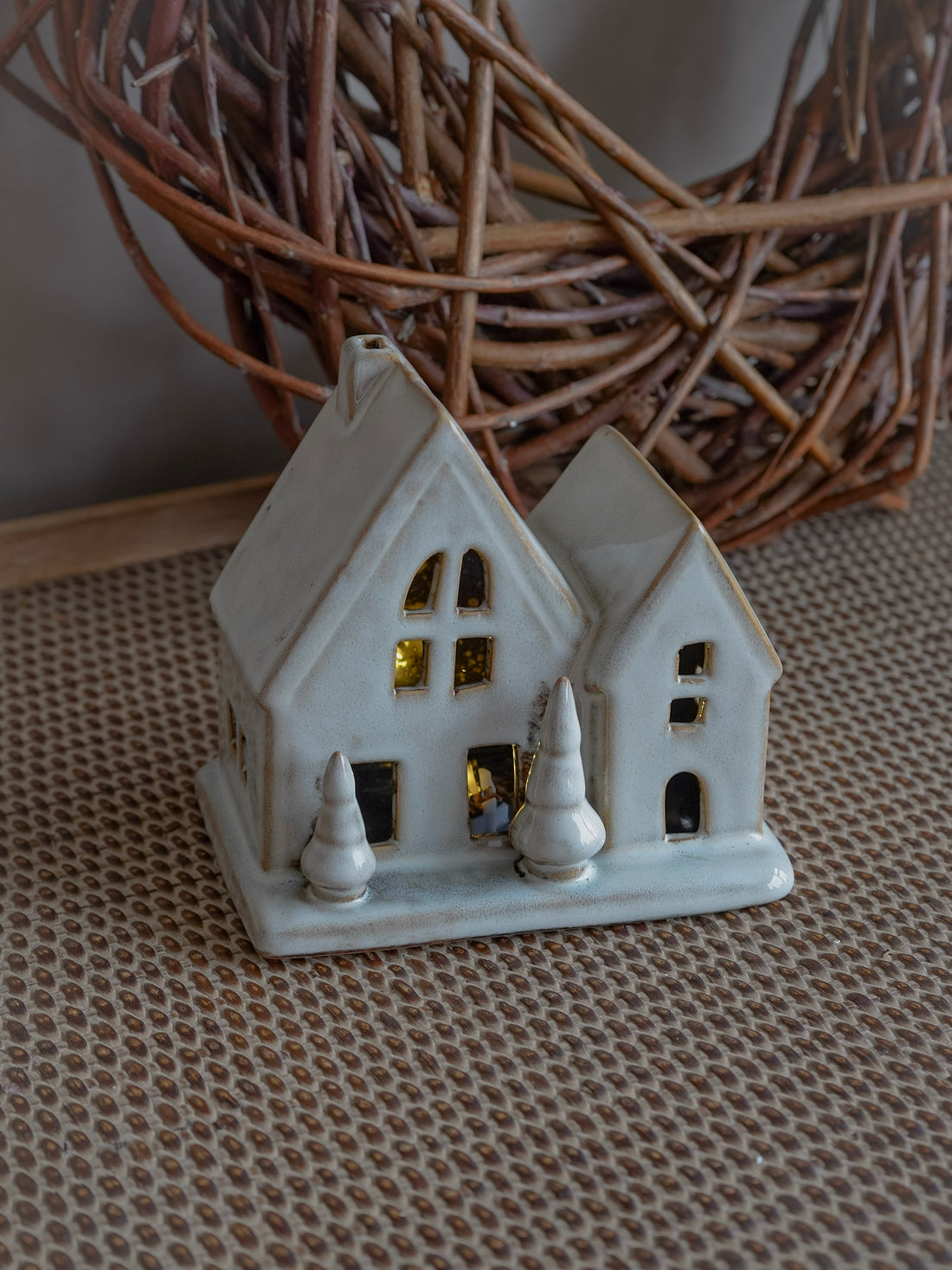 White ceramic house ornament on a textured surface with a woven basket in the background