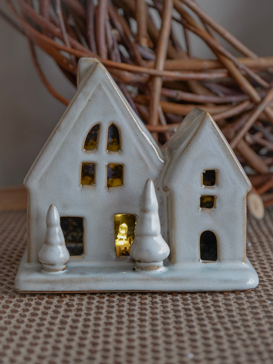 White ceramic house-shaped lantern with lit interior on a textured surface.
